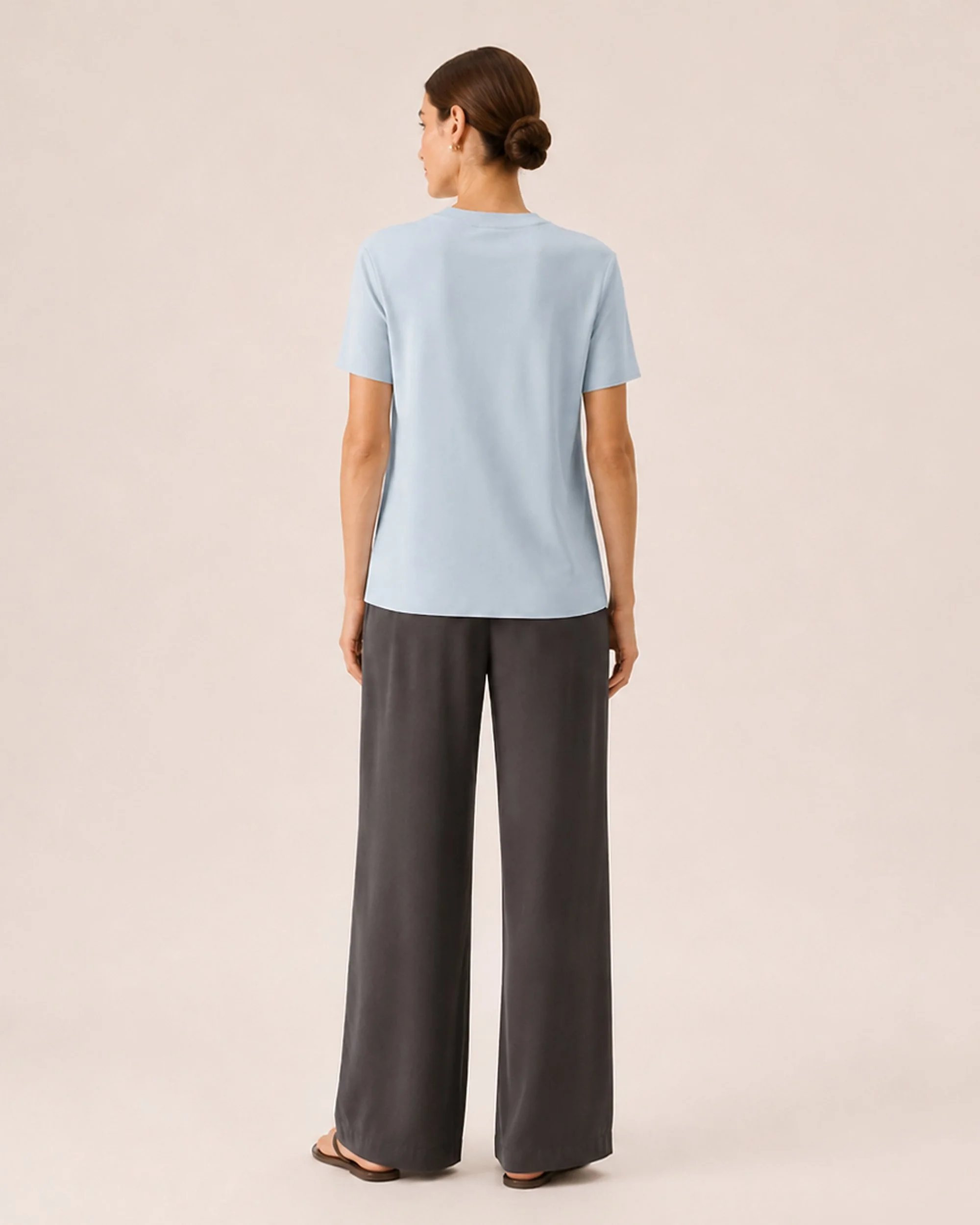 Back view of The Flax Studio blue Silk Crew Neck Top worn with dark trousers.