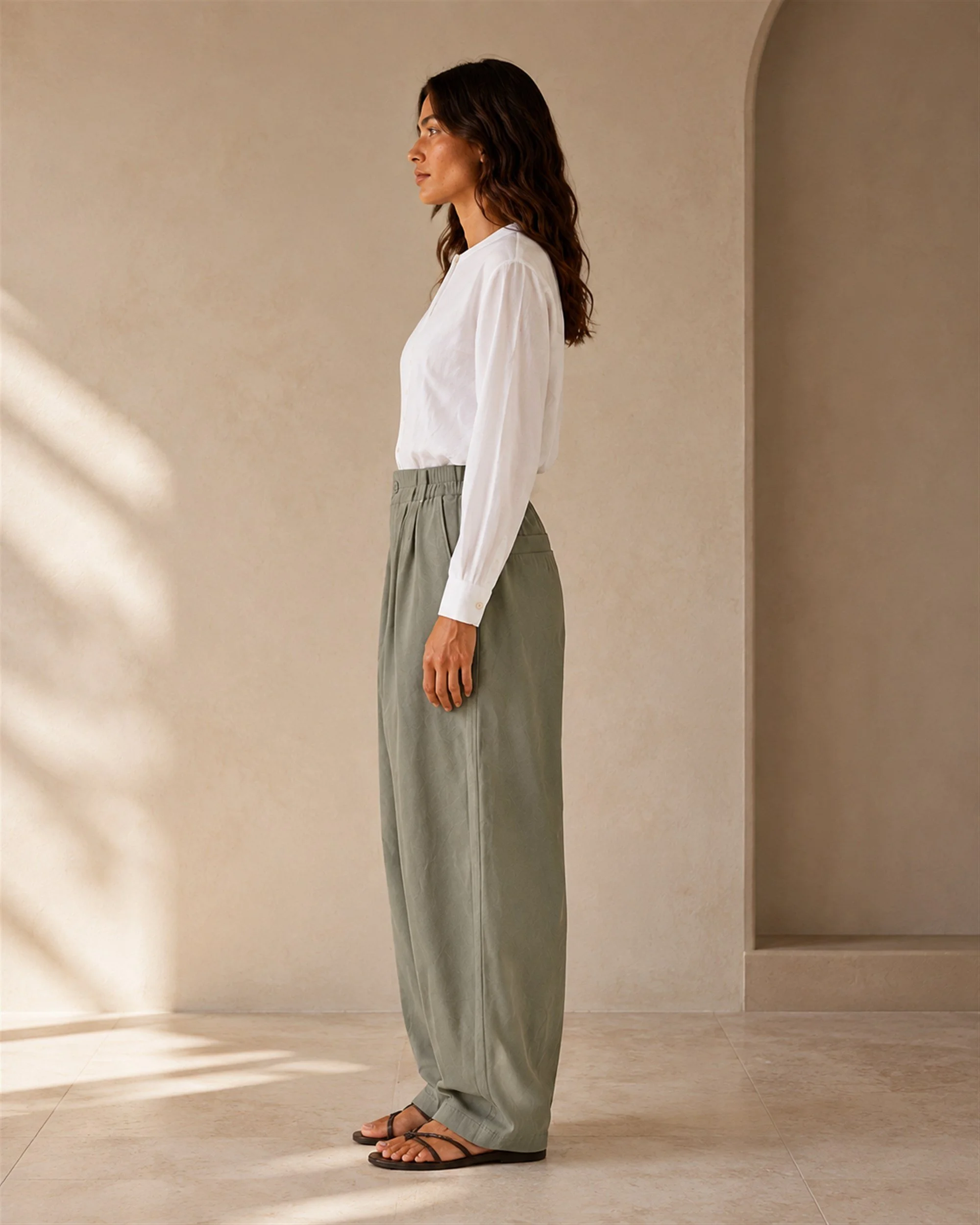 Side view of The Flax Studio khaki Button Front Crepe Pant, showing its curved leg shape and tapered hem.