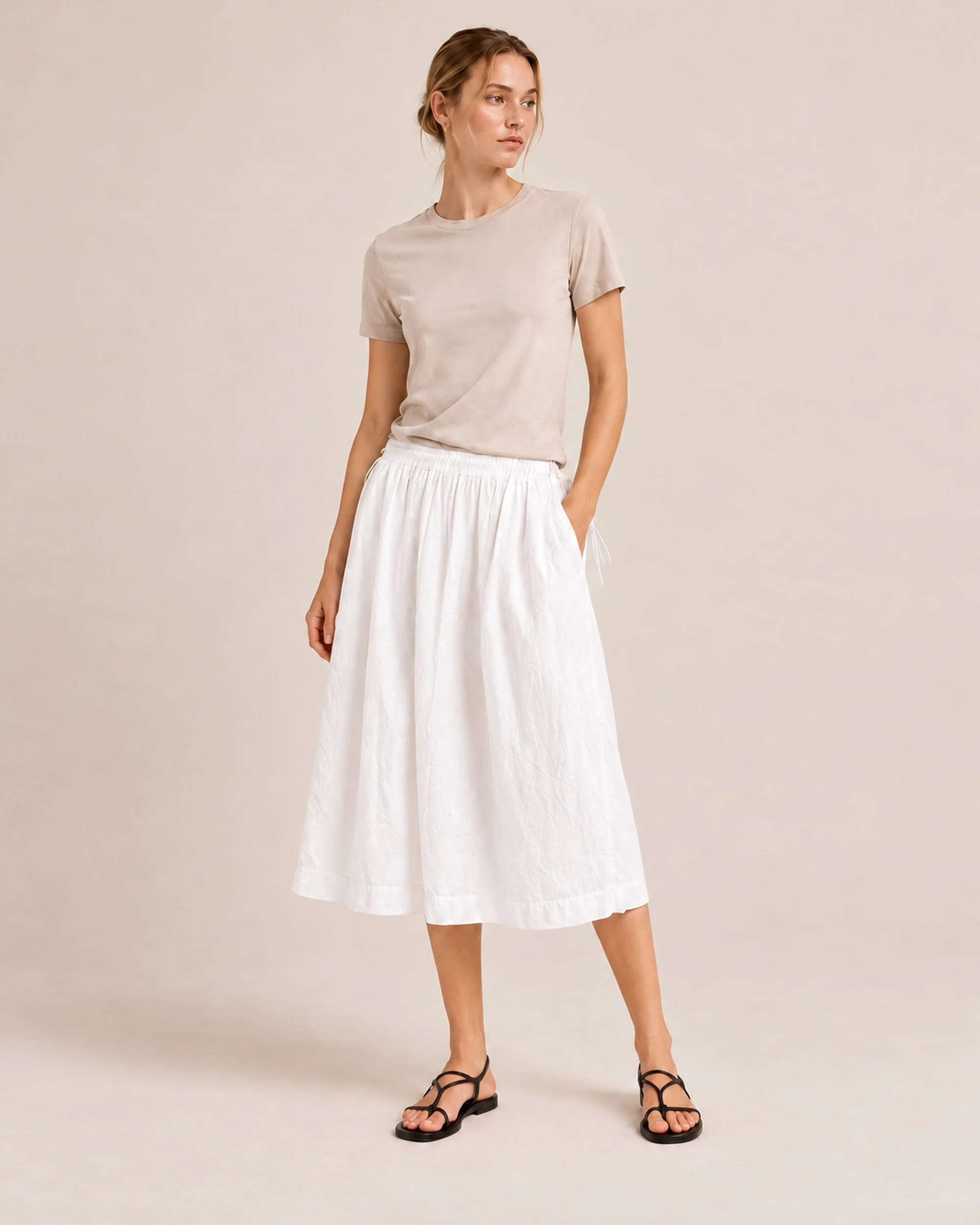 Front view of The Flax Studio white Cotton Tie Skirt, showing its gathered waistband, side ties and midi hem.