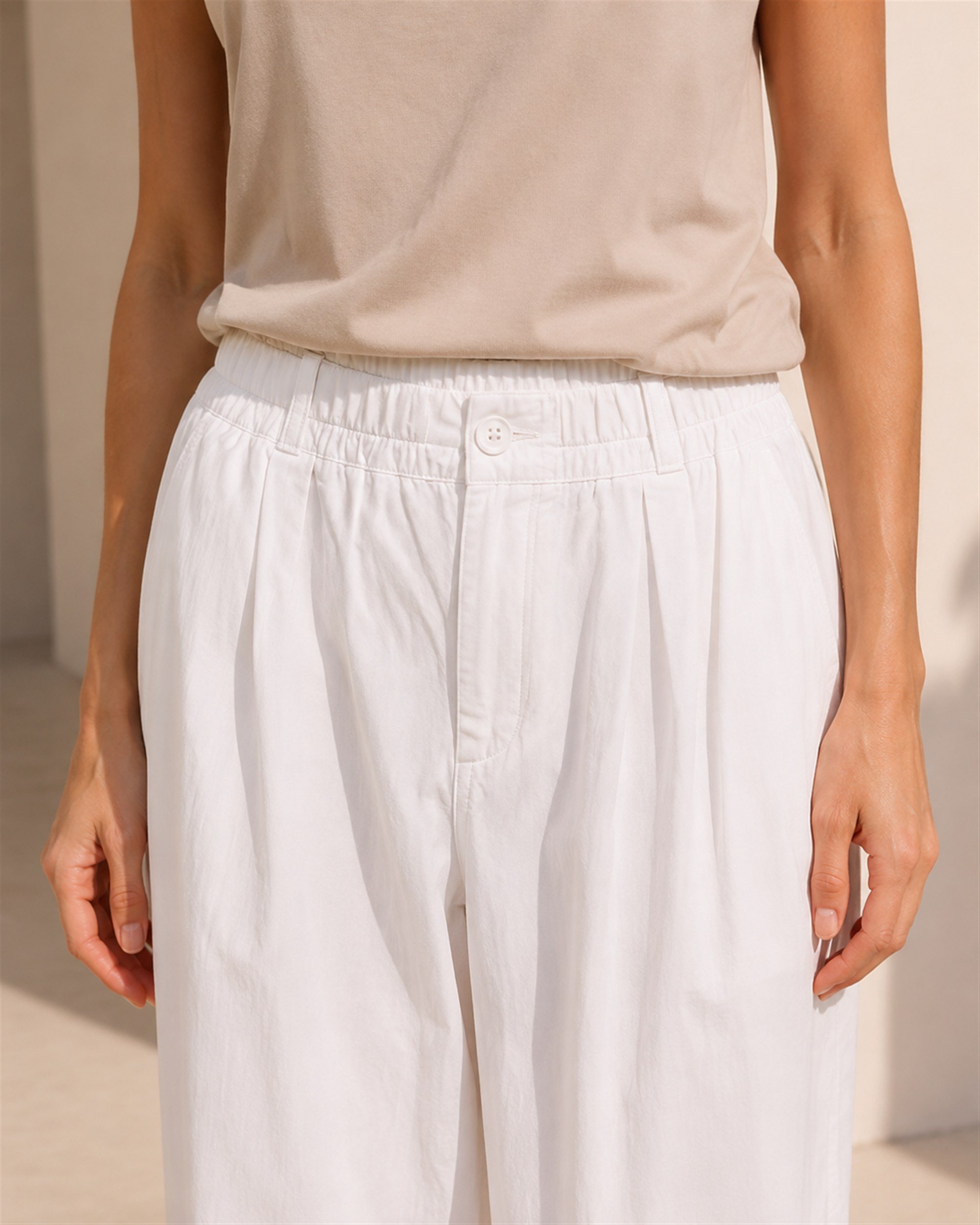 Close-up of The Flax Studio white Button Front Crepe Pant, showing its button fastening, belt loops and gathered waistband.
