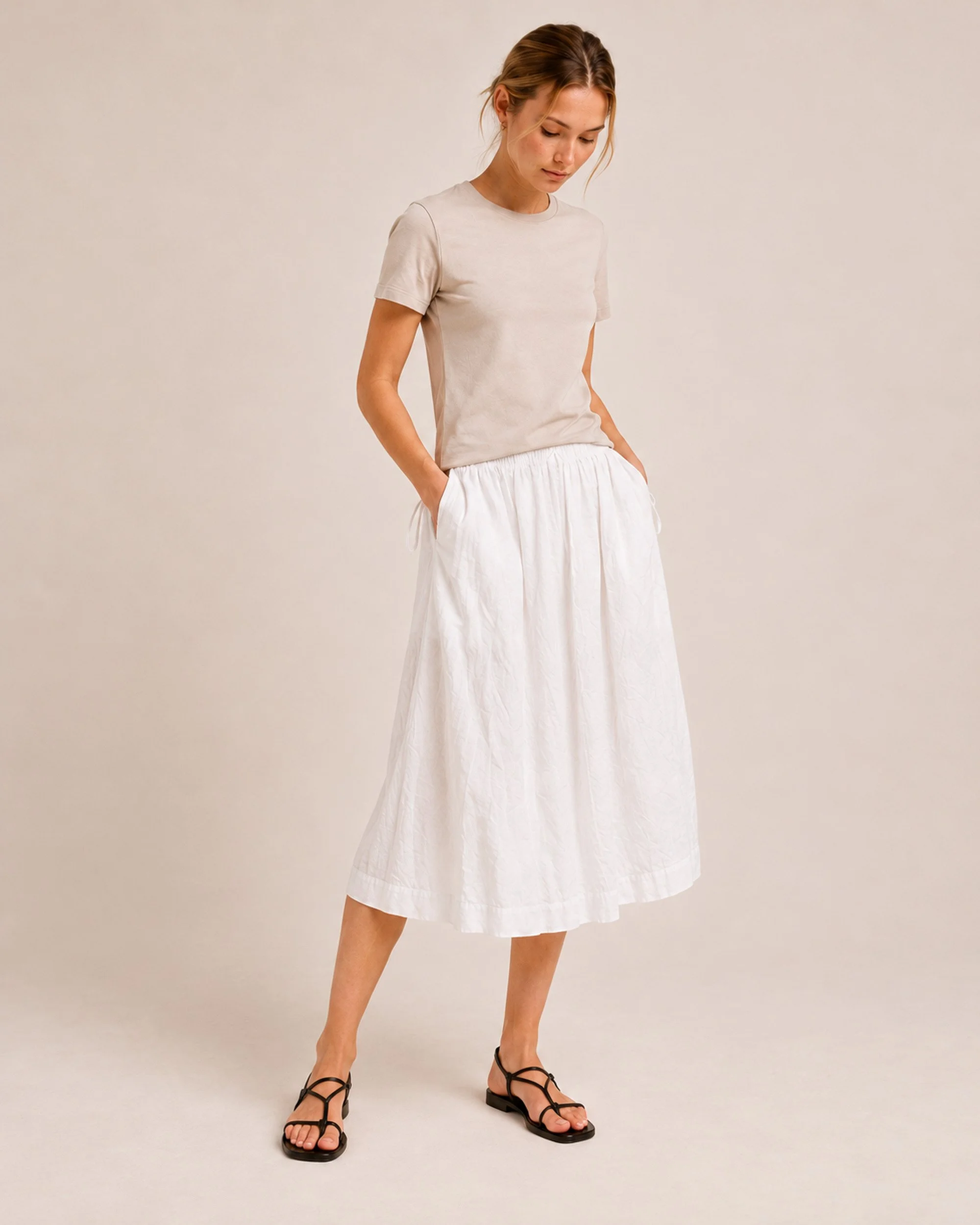 The Flax Studio white Cotton Tie Skirt styled with a sand T-shirt, angled front view showing the side ties and midi silhouette.