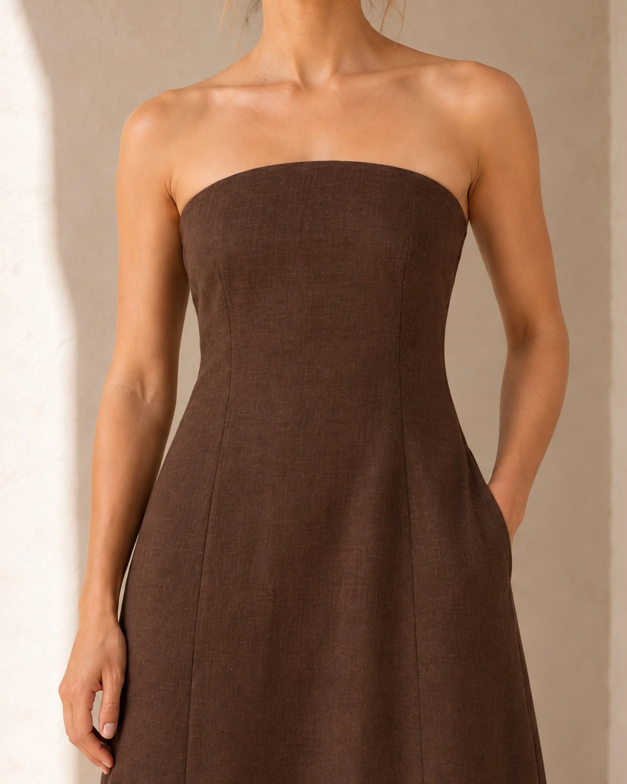 Close-up of the softly rounded neckline and chocolate linen-cotton fabric on The Flax Studio Strapless Linen Dress.