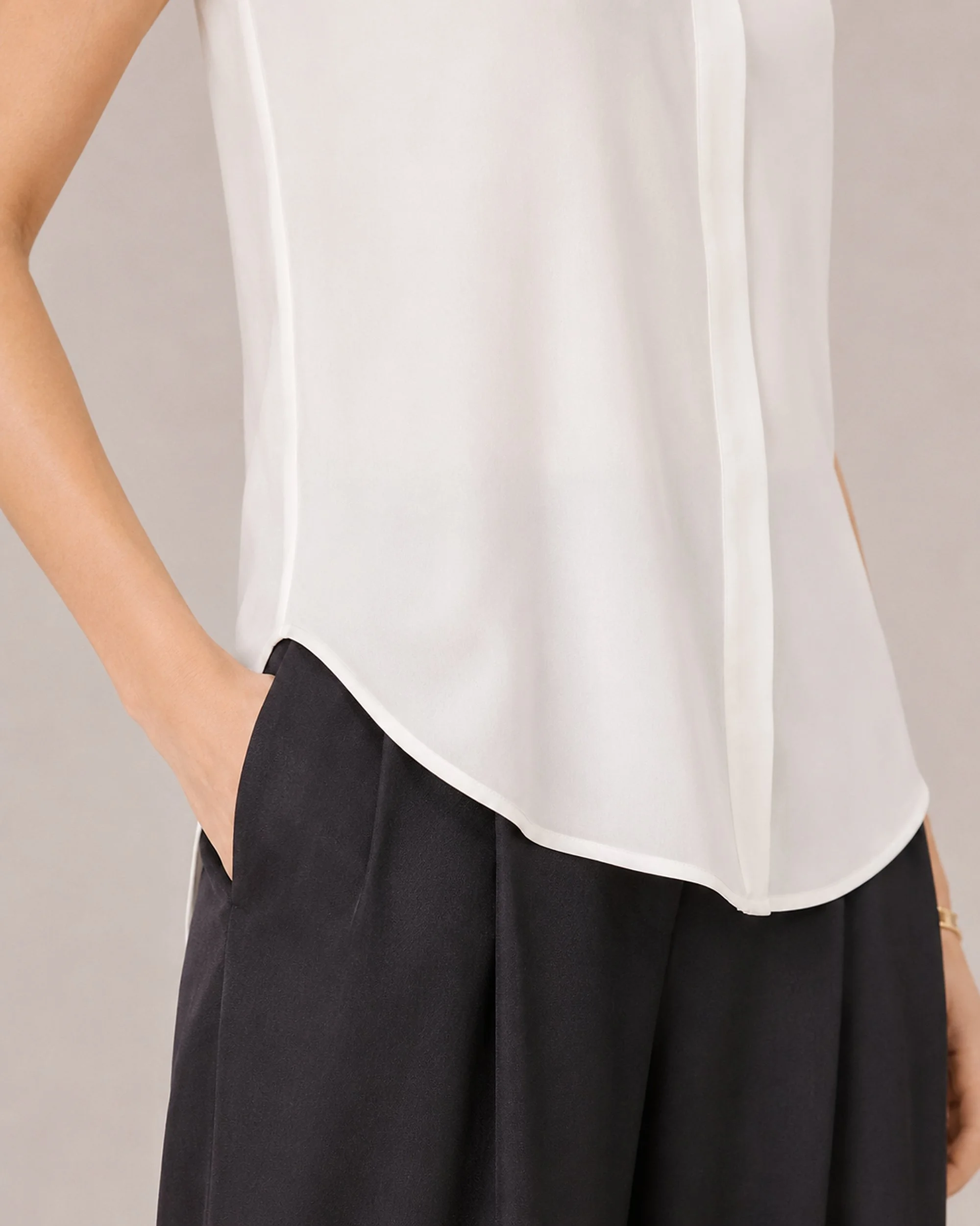 Close-up of the curved hem and fluid silk drape on The Flax Studio white Mulberry Silk Sleeveless Blouse.
