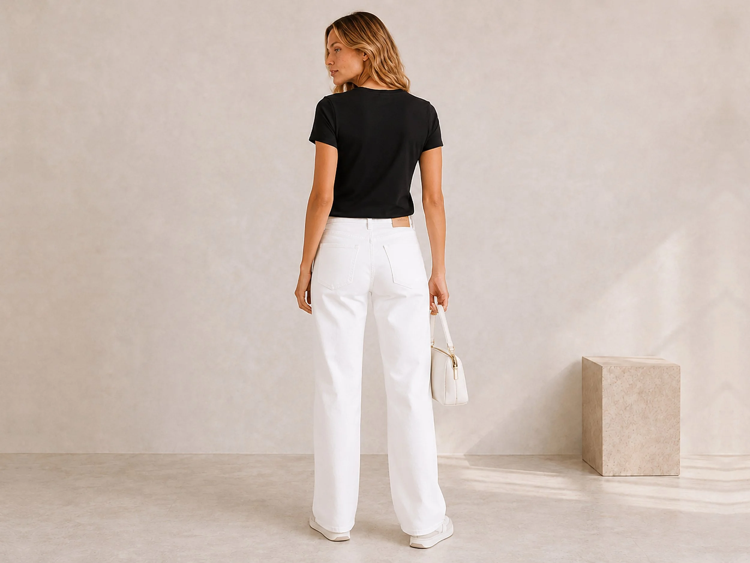 Back view of The Flax Studio black mercerised cotton T-shirt worn with white trousers.