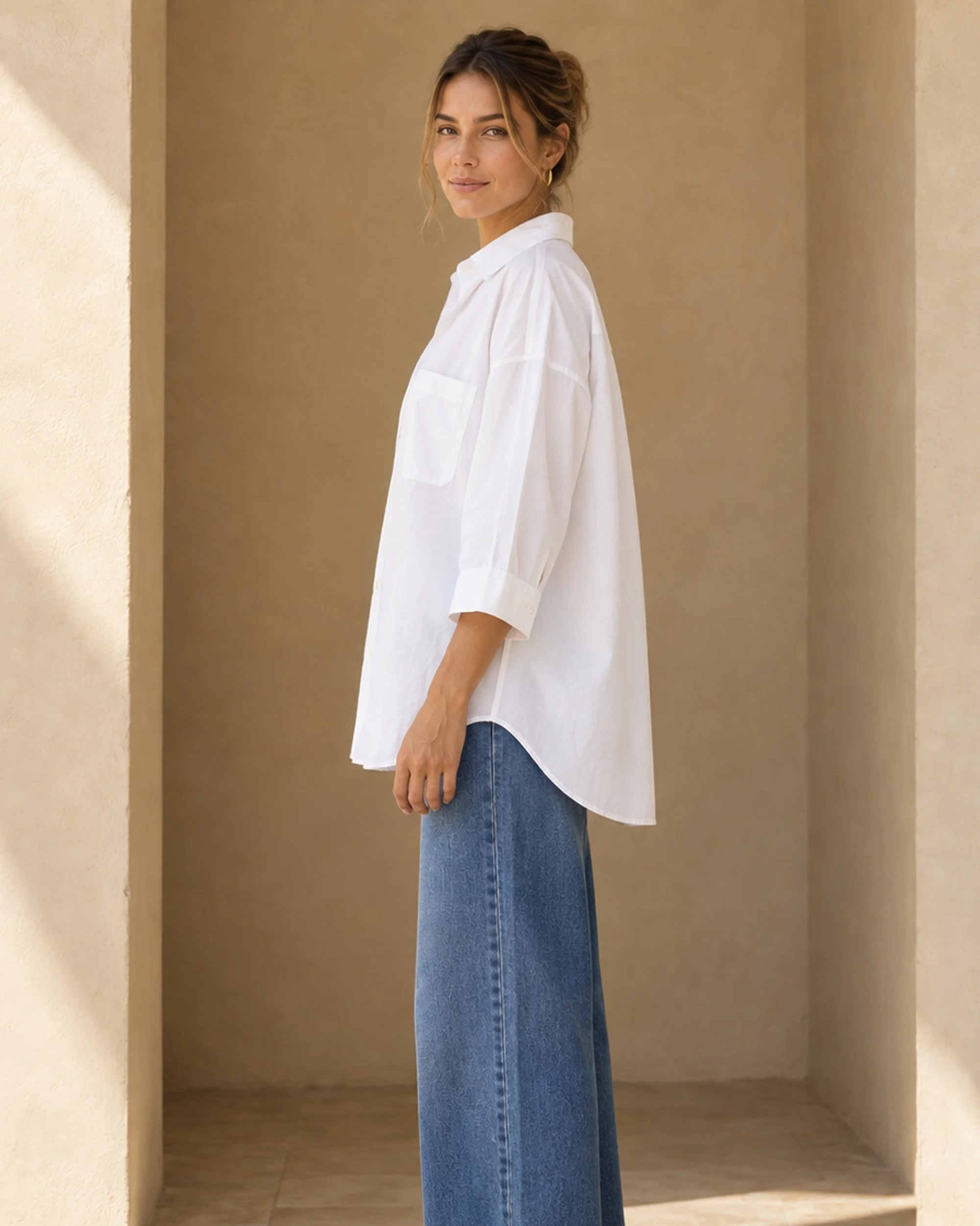 Side view of the white Oversized Cotton Shirt, showing its loose shape and curved hem.