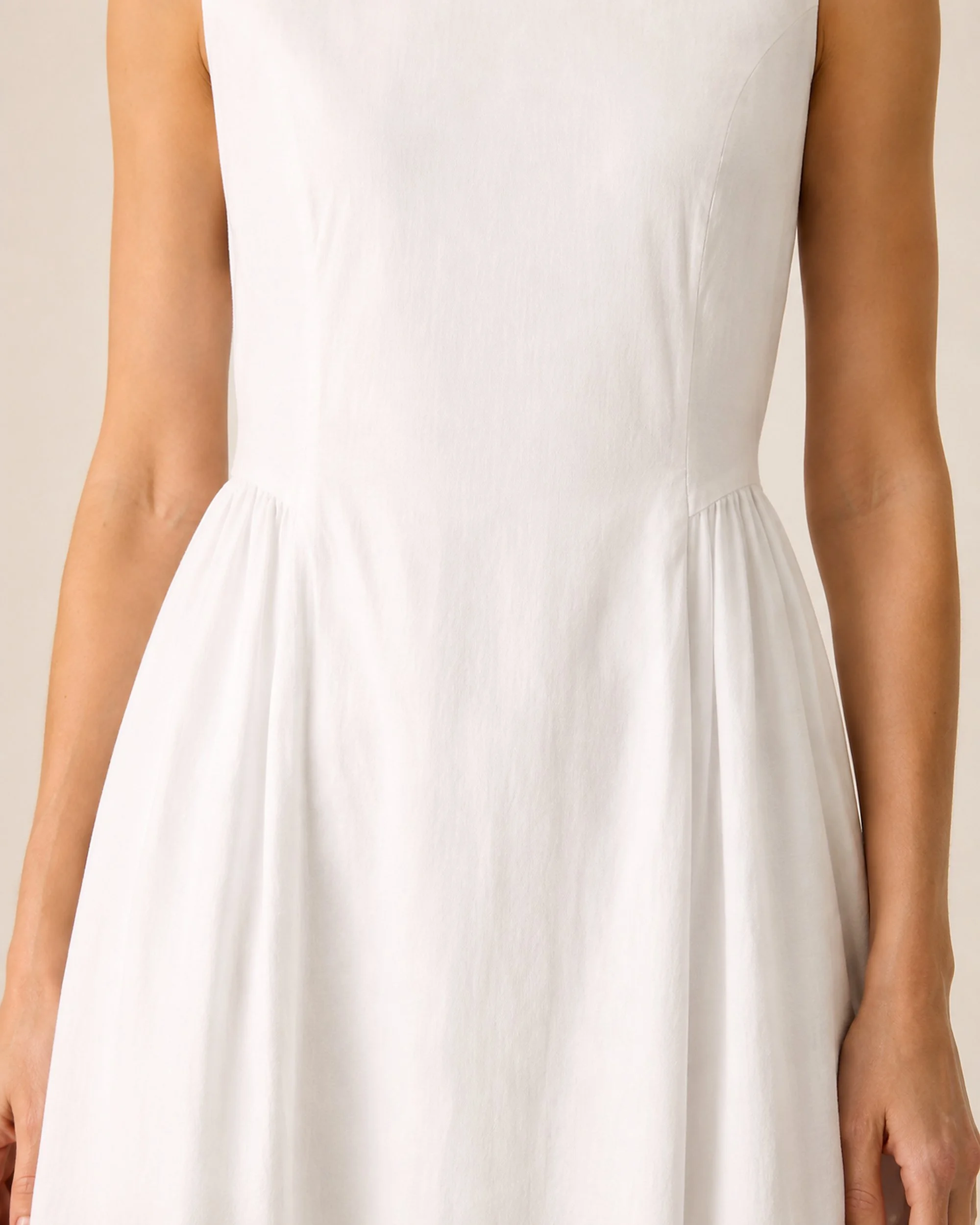 Close-up of the waist shaping and skirt pleats on The Flax Studio white Tailored Dress.