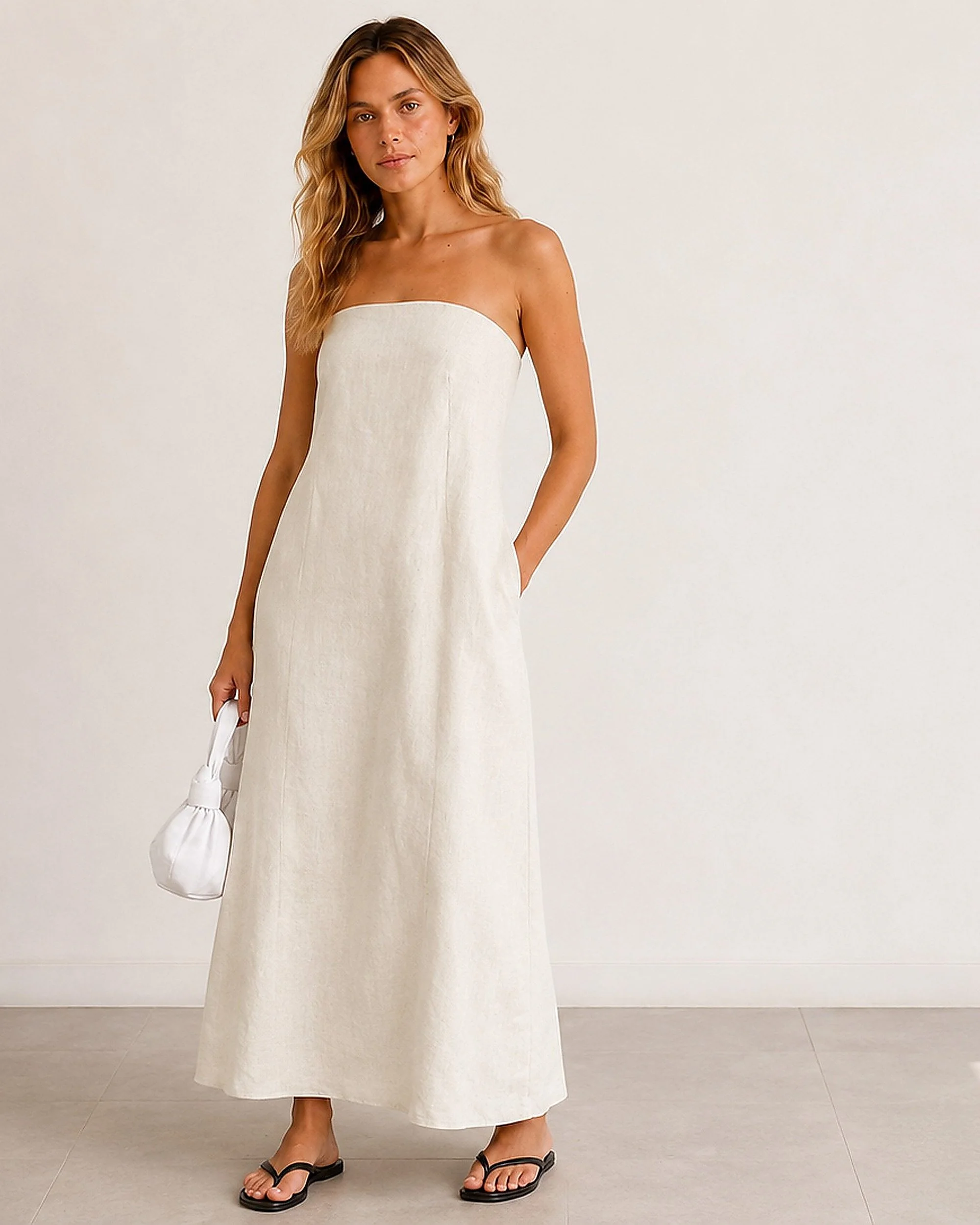 The Flax Studio Sand Strapless Linen Dress worn with one hand in a side pocket, showing its relaxed maxi silhouette.