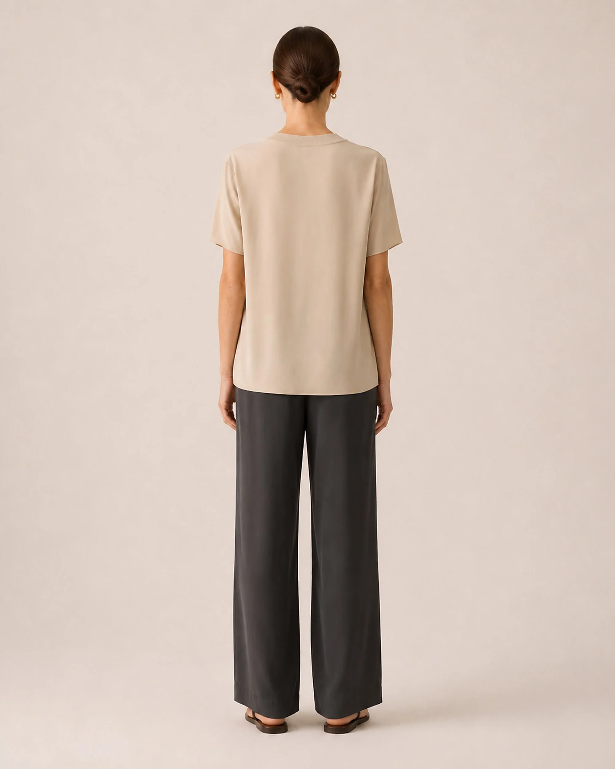 Back view of The Flax Studio beige Silk Crew Neck Top worn with dark trousers.