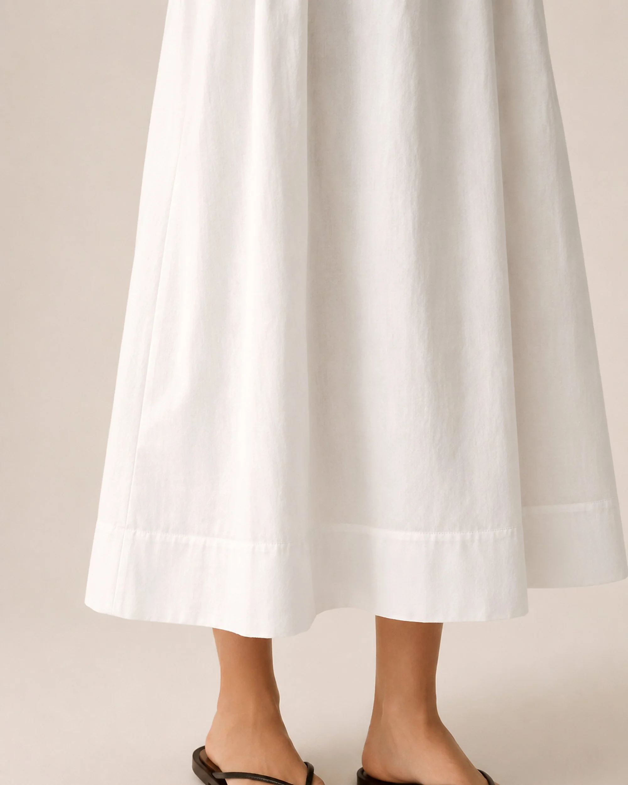 Hem detail of The Flax Studio white Tailored Dress, showing the flared skirt and stitched finish.