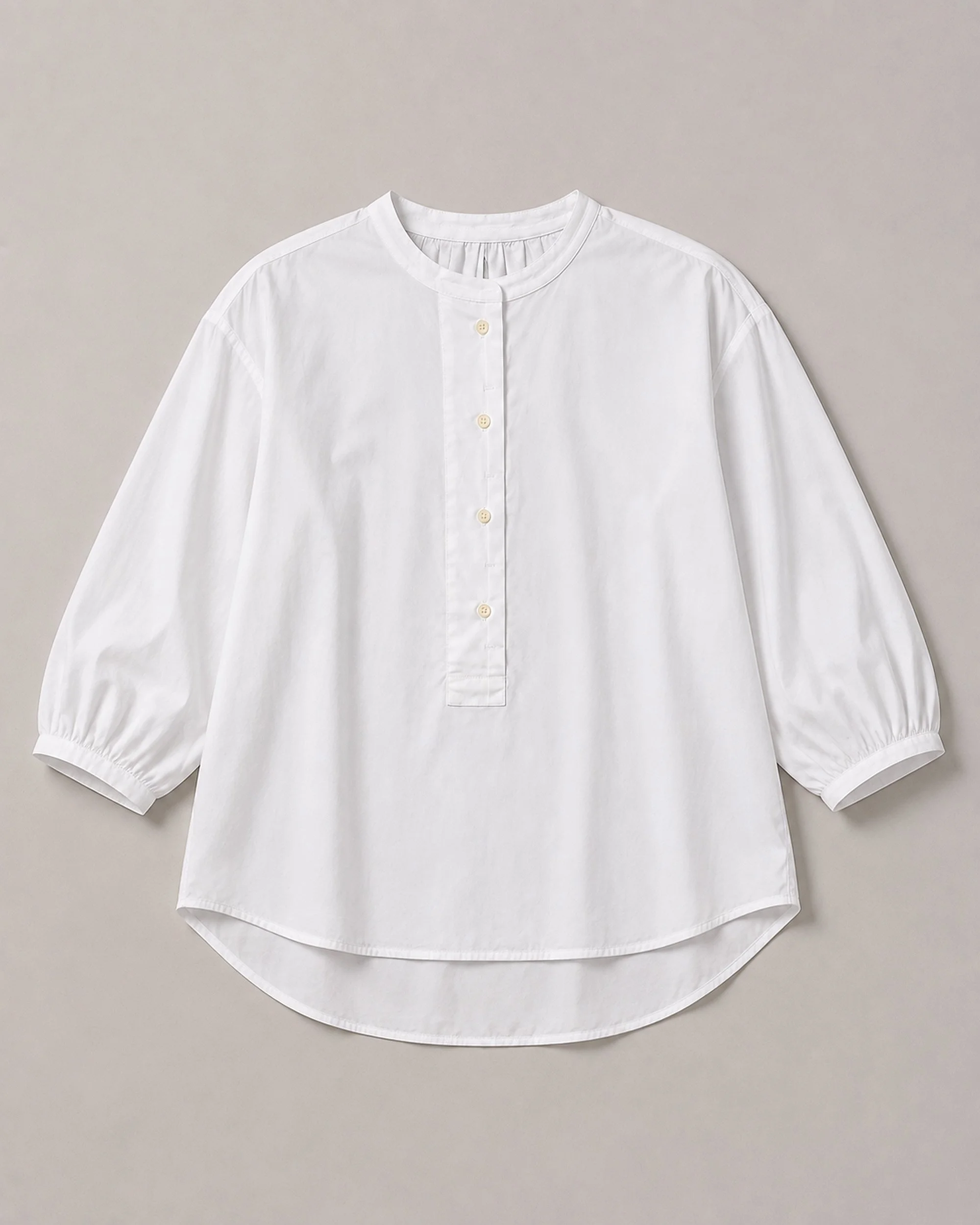 The Flax Studio white Voluminous Cotton Top laid flat, showing the button placket, gathered cuffs and curved hem.