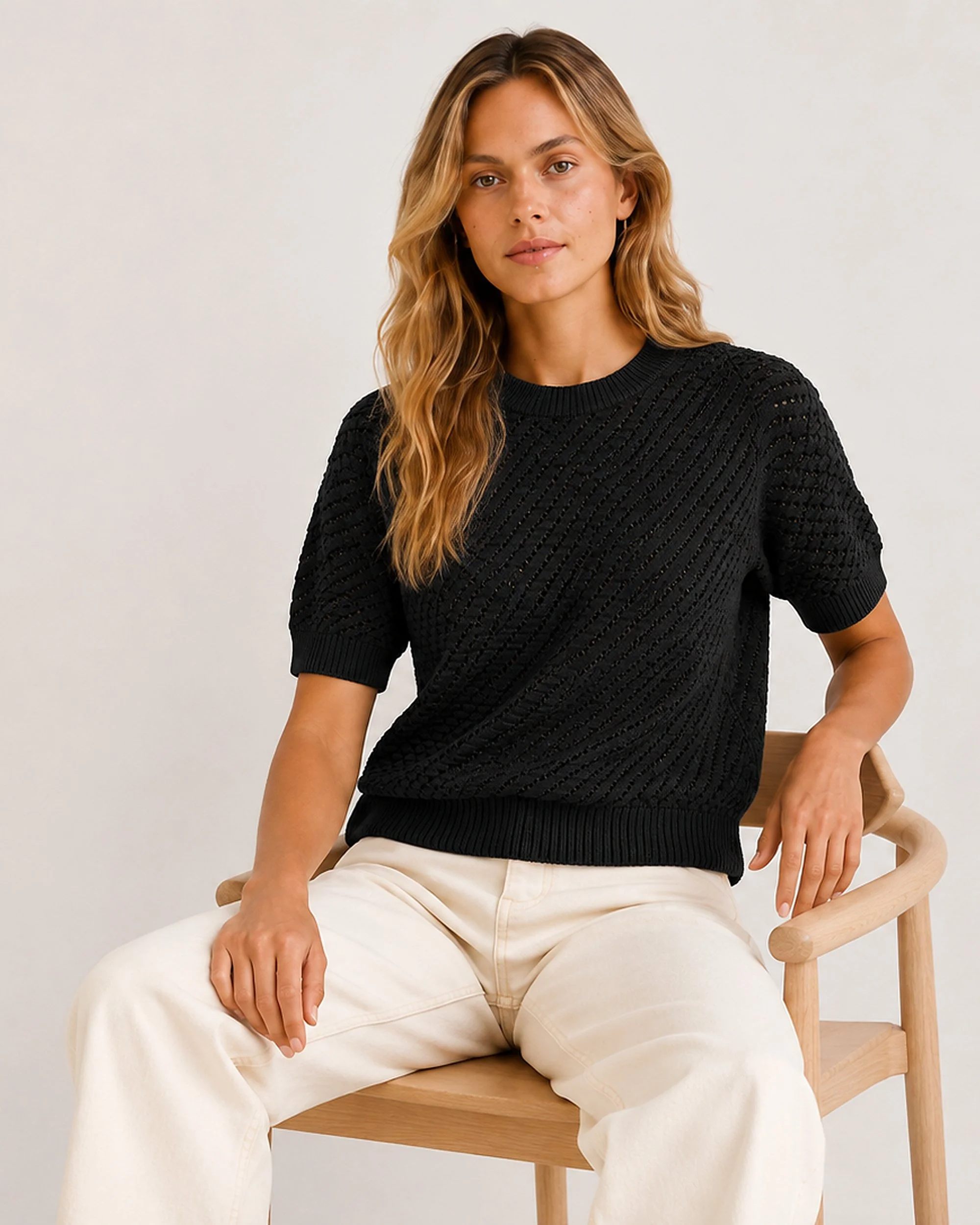 The Flax Studio black Mulberry Silk-Cotton Pointelle Knit worn in a seated pose with light trousers.