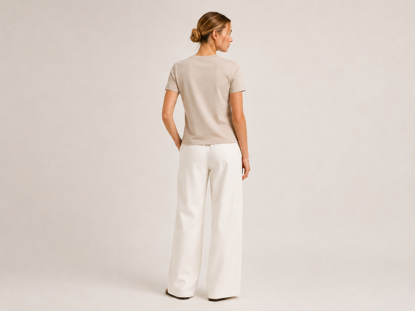 Back view of The Flax Studio sand mercerised cotton T-shirt worn with white trousers.