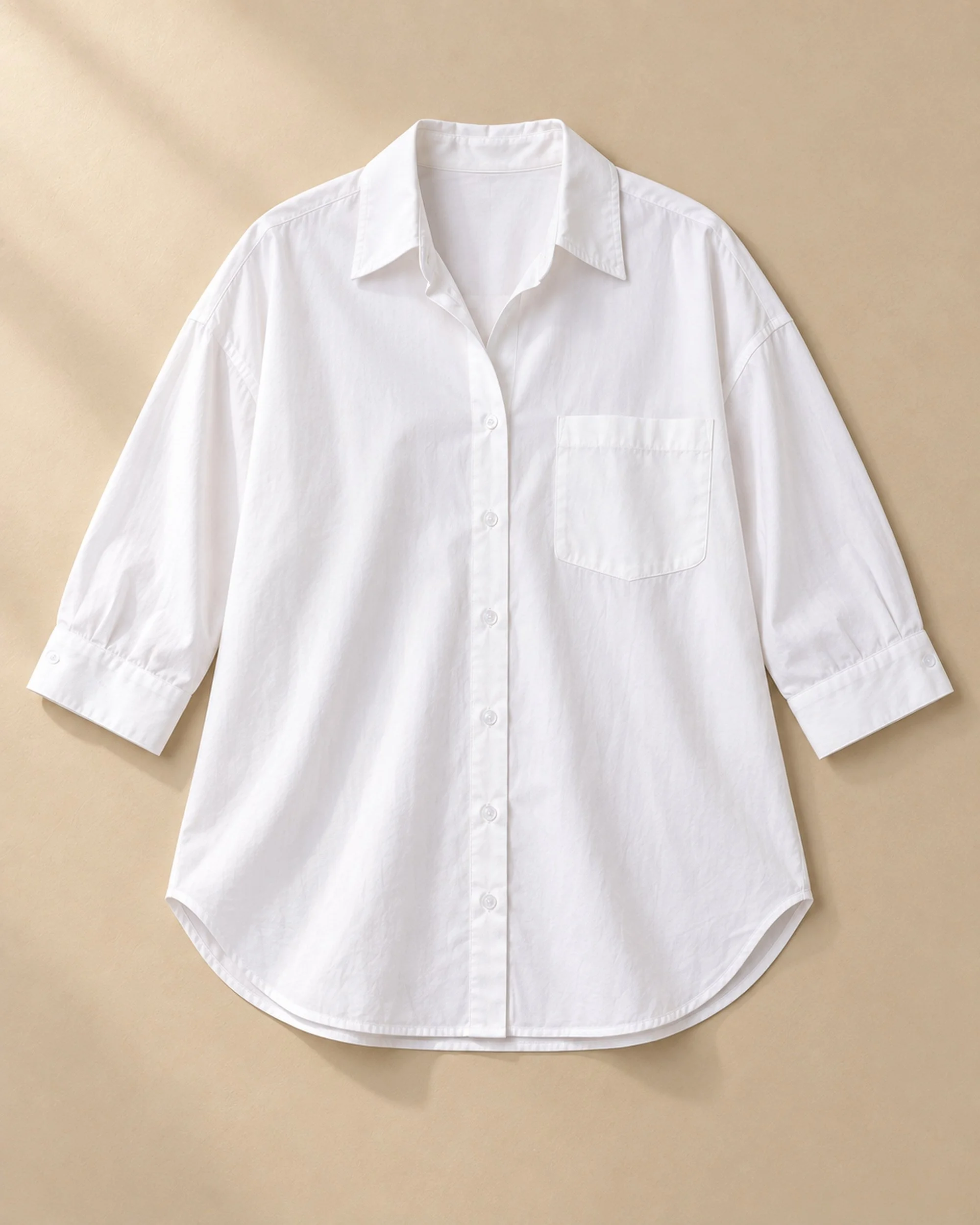 Flat lay of the white Oversized Cotton Shirt, showing its collar, chest pocket, button cuffs and curved hem.