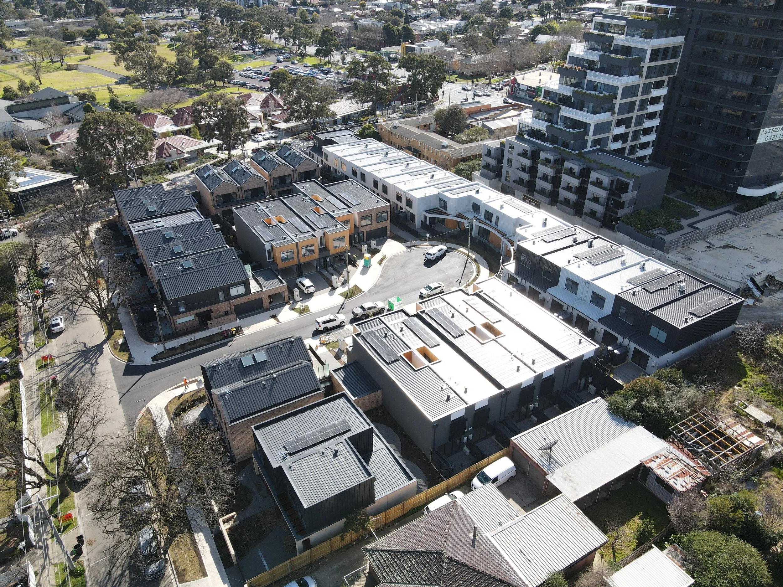 Aerial view of a city neighborhood with modern and traditional houses, tall apartment buildings, trees, parking lots, and streets