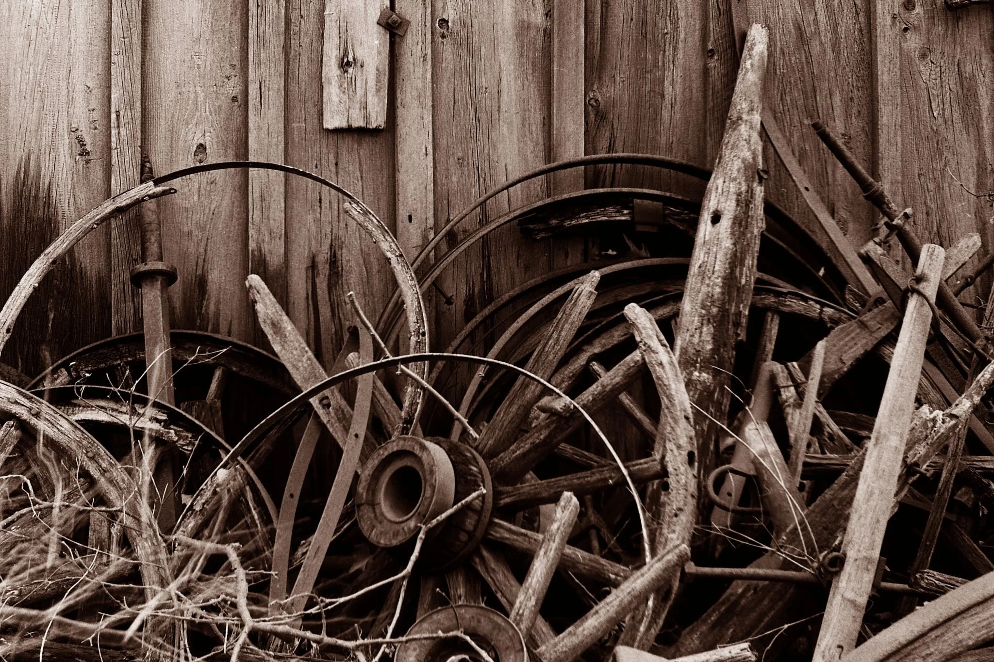 A large pile of old, weathered wagon wheels and wooden tools stacked against a wooden wall.
