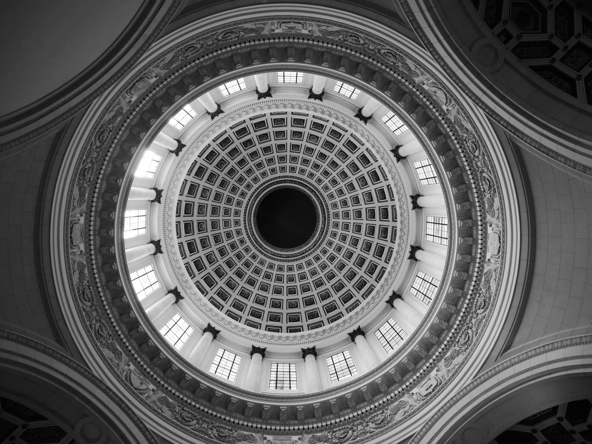 Looking up at the ornate dome ceiling of a grand building, featuring intricate decorations, columns, and large windows allowing natural light.