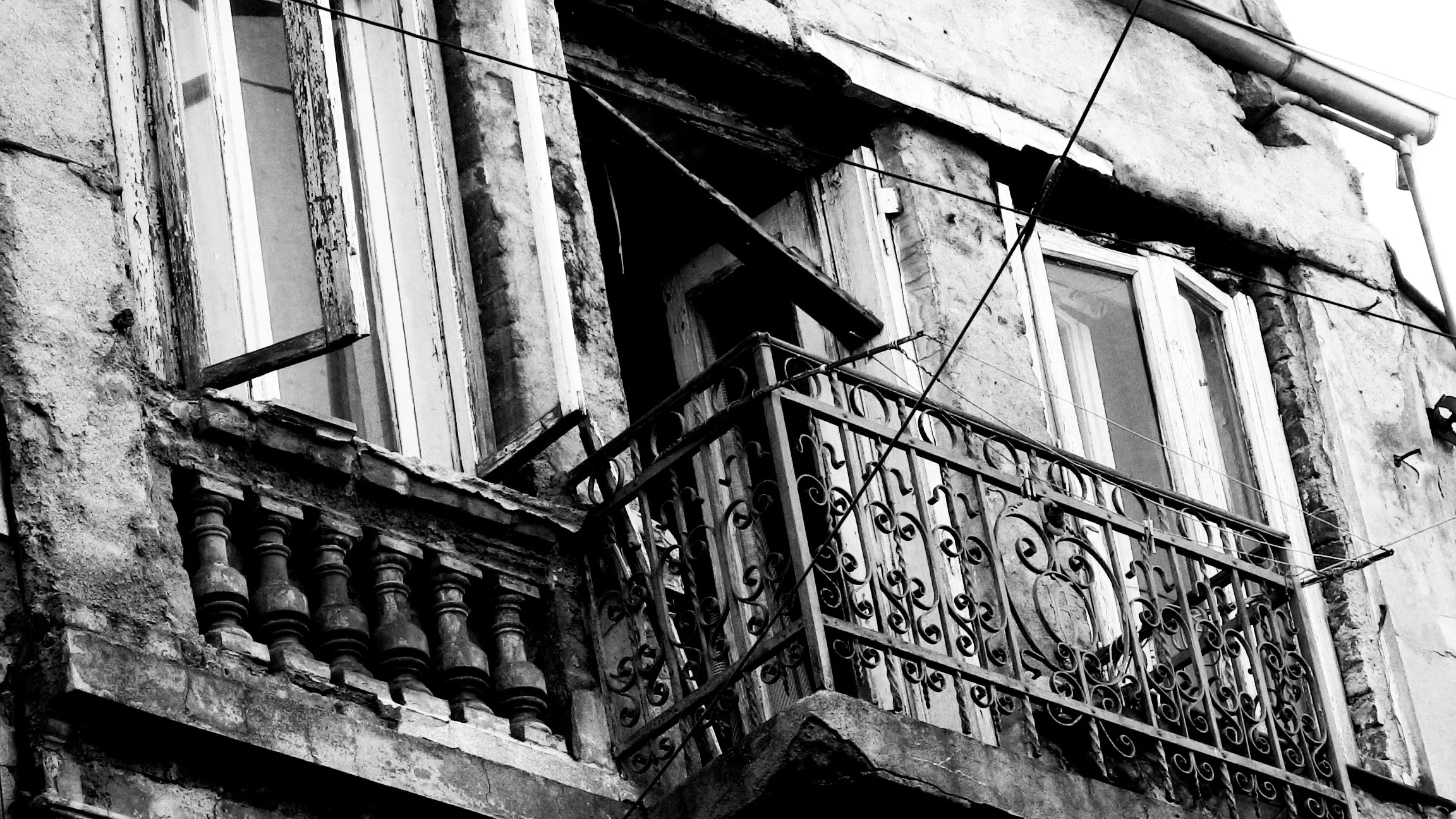 Black and white photo of an old building facade with worn windows and ornate balcony railings.