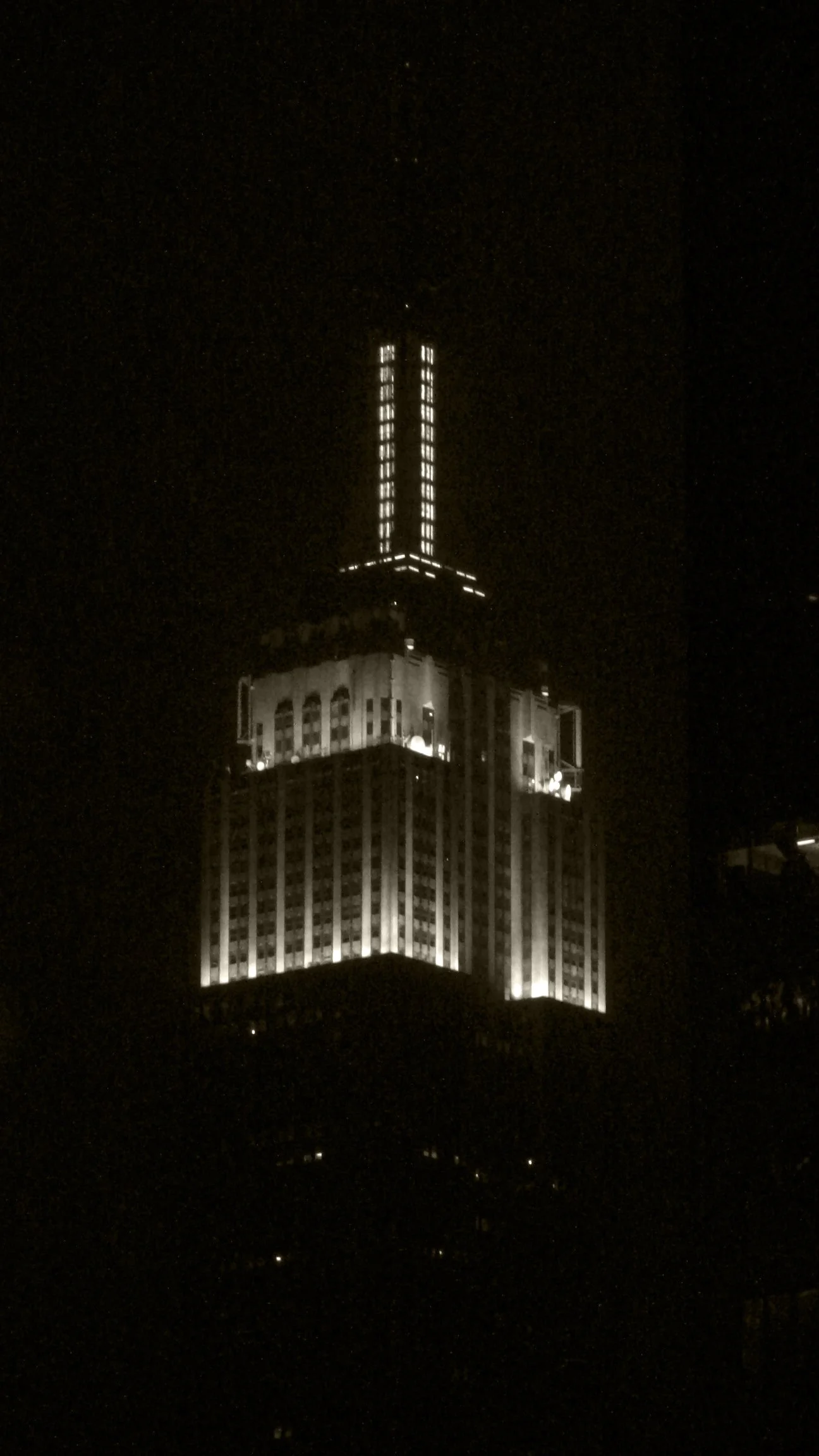 Night view of a tall, illuminated skyscraper with vertical bright lines and lit windows.