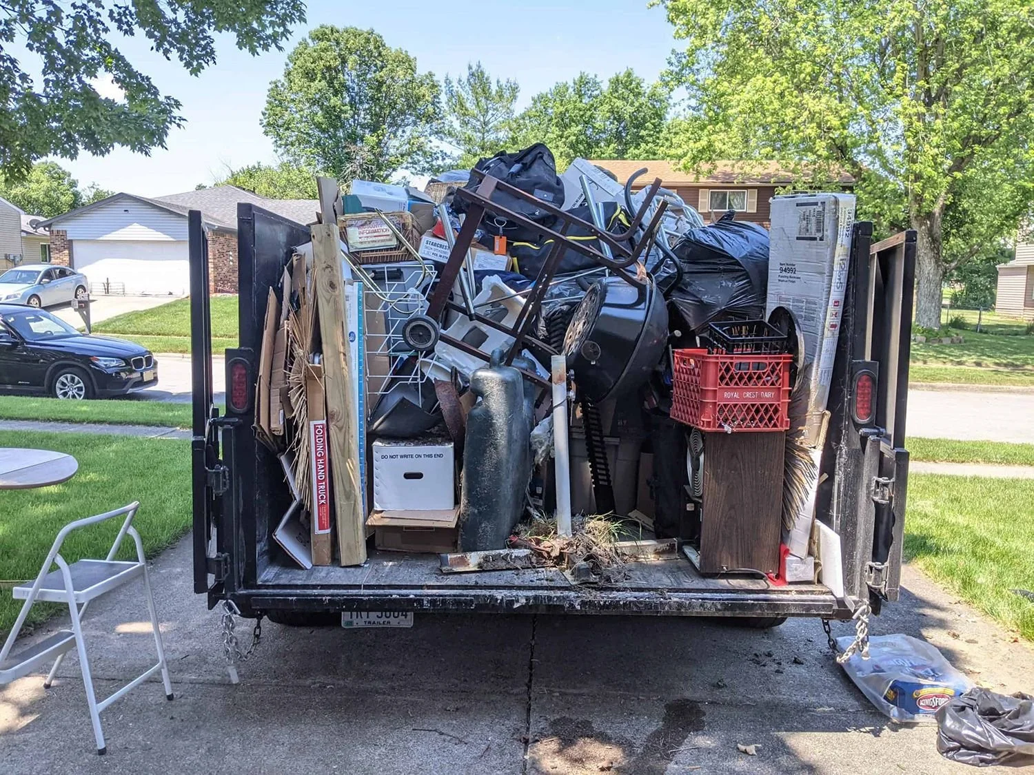 Overfilled moving truck with household items, furniture, and boxes, parked in a suburban neighborhood with green lawns and trees.