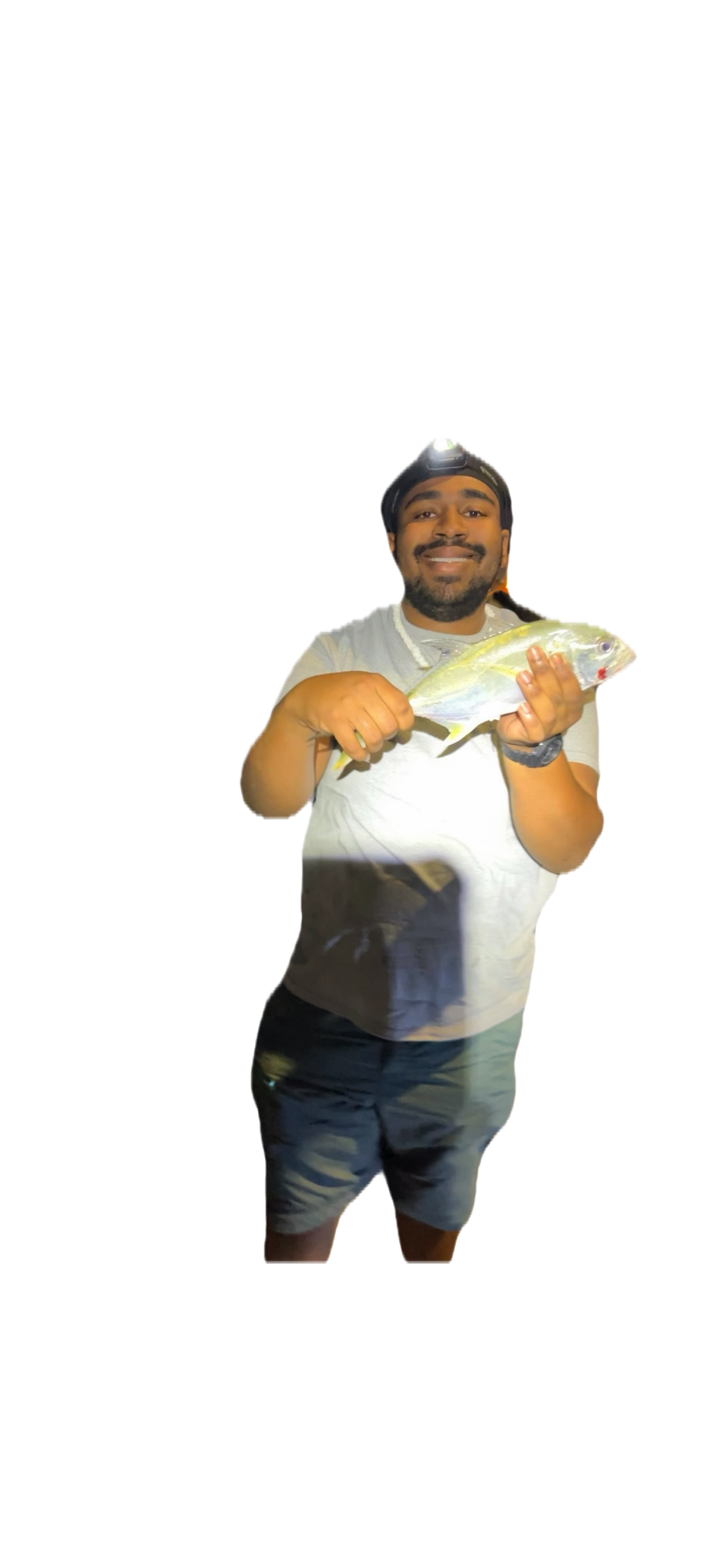 A man with a beard, wearing a headlamp, a gray t-shirt, and shorts, smiling and holding a fish.