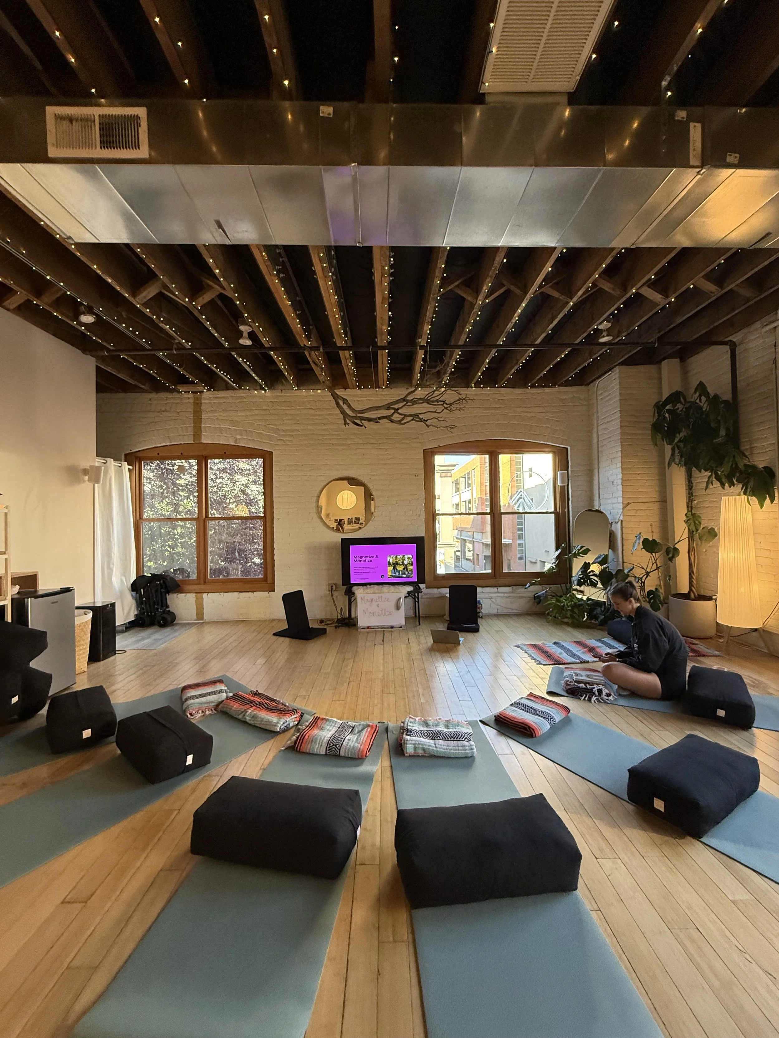 An indoor space set up for yoga or meditation with blue mats and black cushions on a wooden floor. At Pine and Prism, a wellness hub where Jane teaches classes on guided imagery.