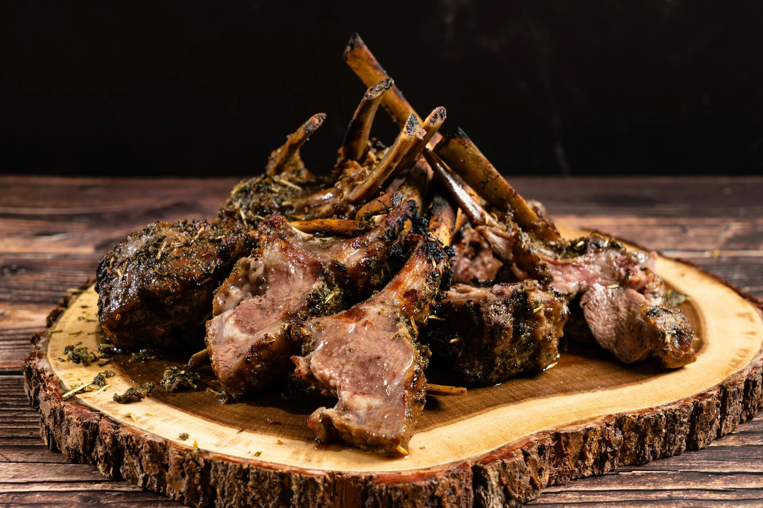 Cooked herb-seasoned lamb chops piled on a wooden serving board
