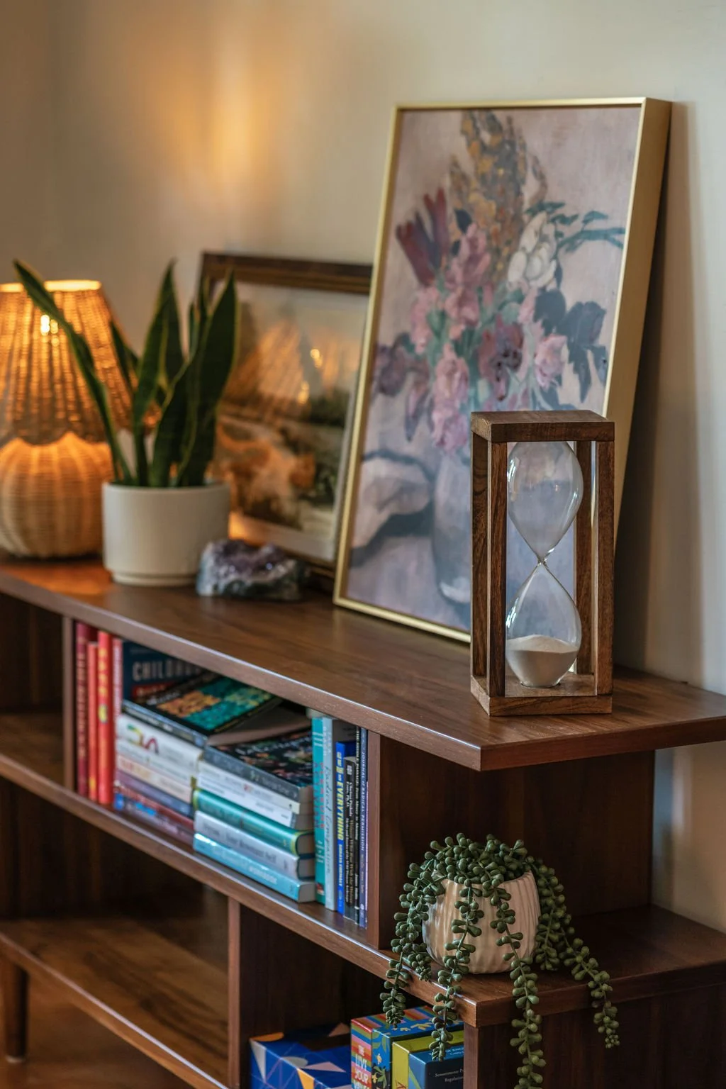 Wooden bookshelf with plants, artwork, books, and an hourglass