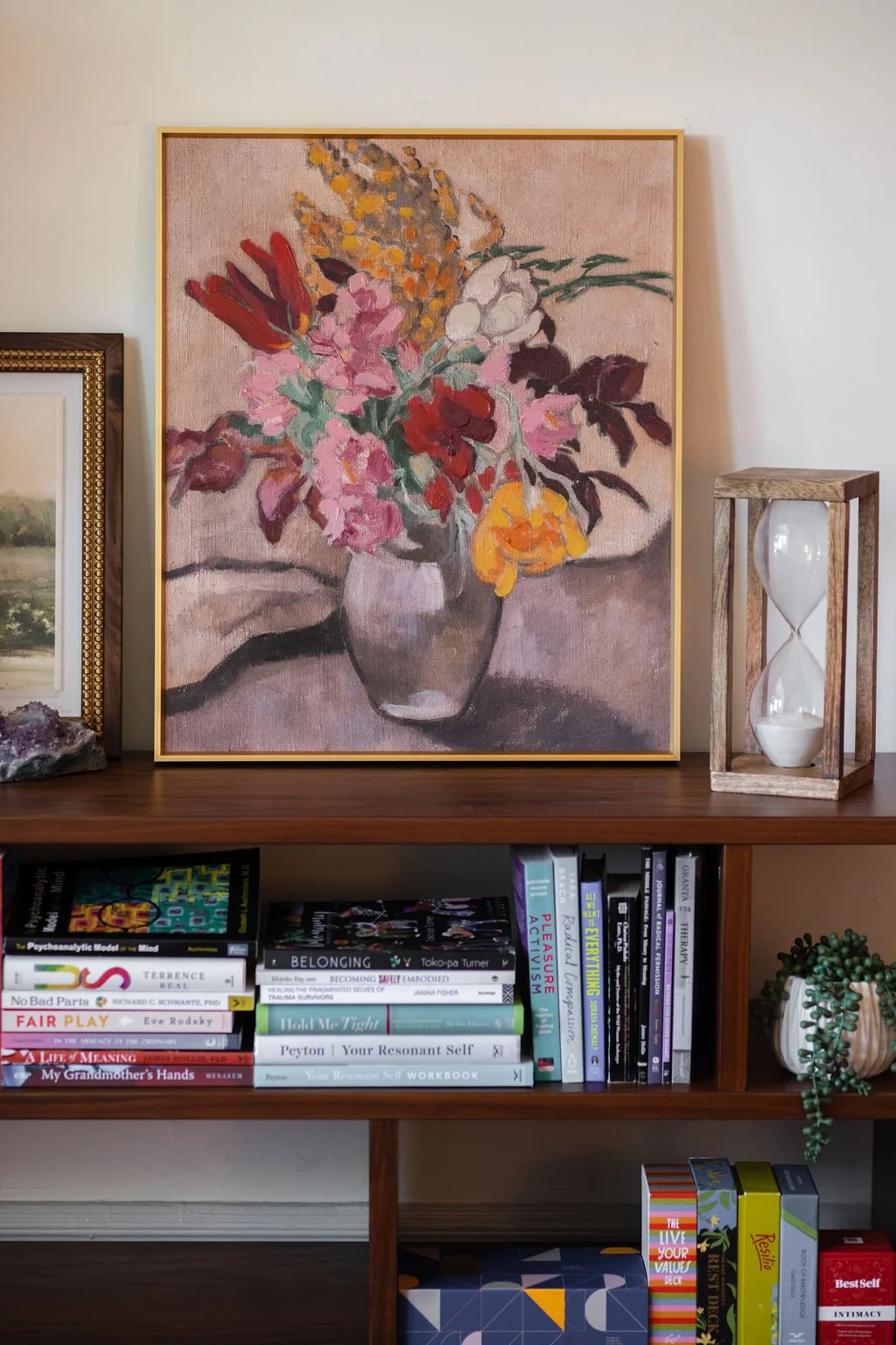 Painting of a colorful flower bouquet in a vase on a wooden shelf, with decorative items and books.