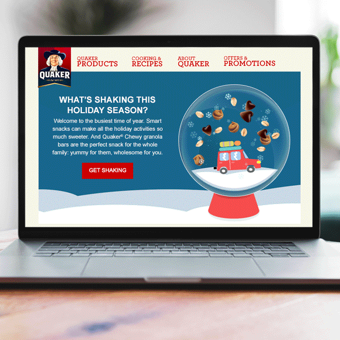 A laptop screen displaying Quaker holiday snack promotion with a snow globe containing a red truck and various nuts inside.