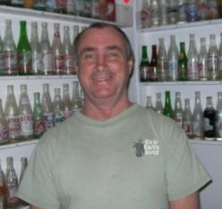 A man standing in front of shelves filled with various glass bottles, smiling at the camera.