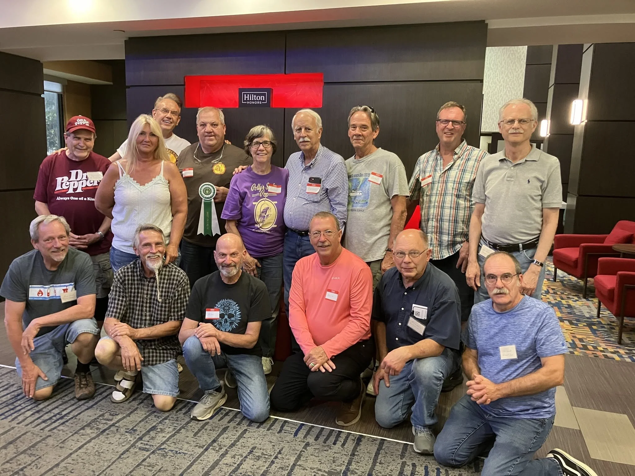 Group of people gathered in a conference room at the Hilton Honors hotel, some standing and some kneeling, posing for a group photo.