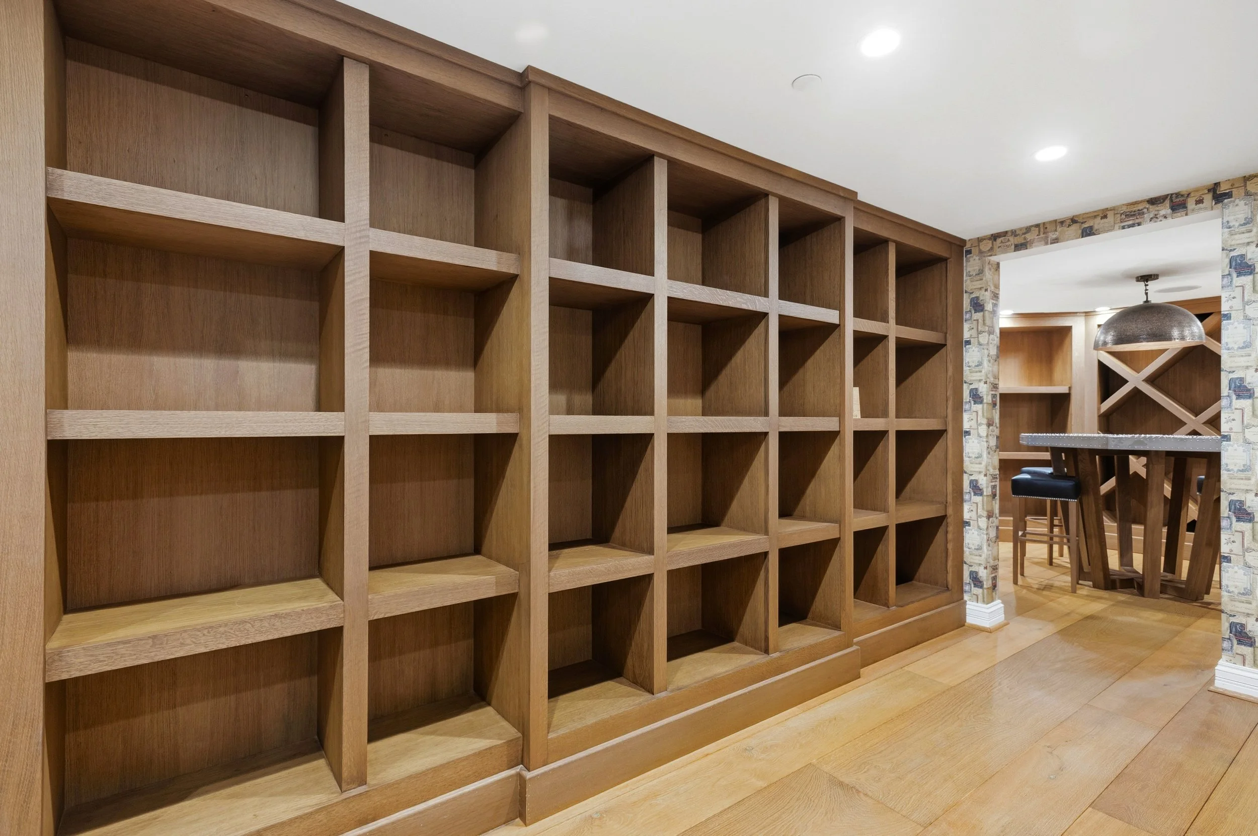 Empty wooden bookshelf in a room with wood flooring and a dining area visible in the background.
