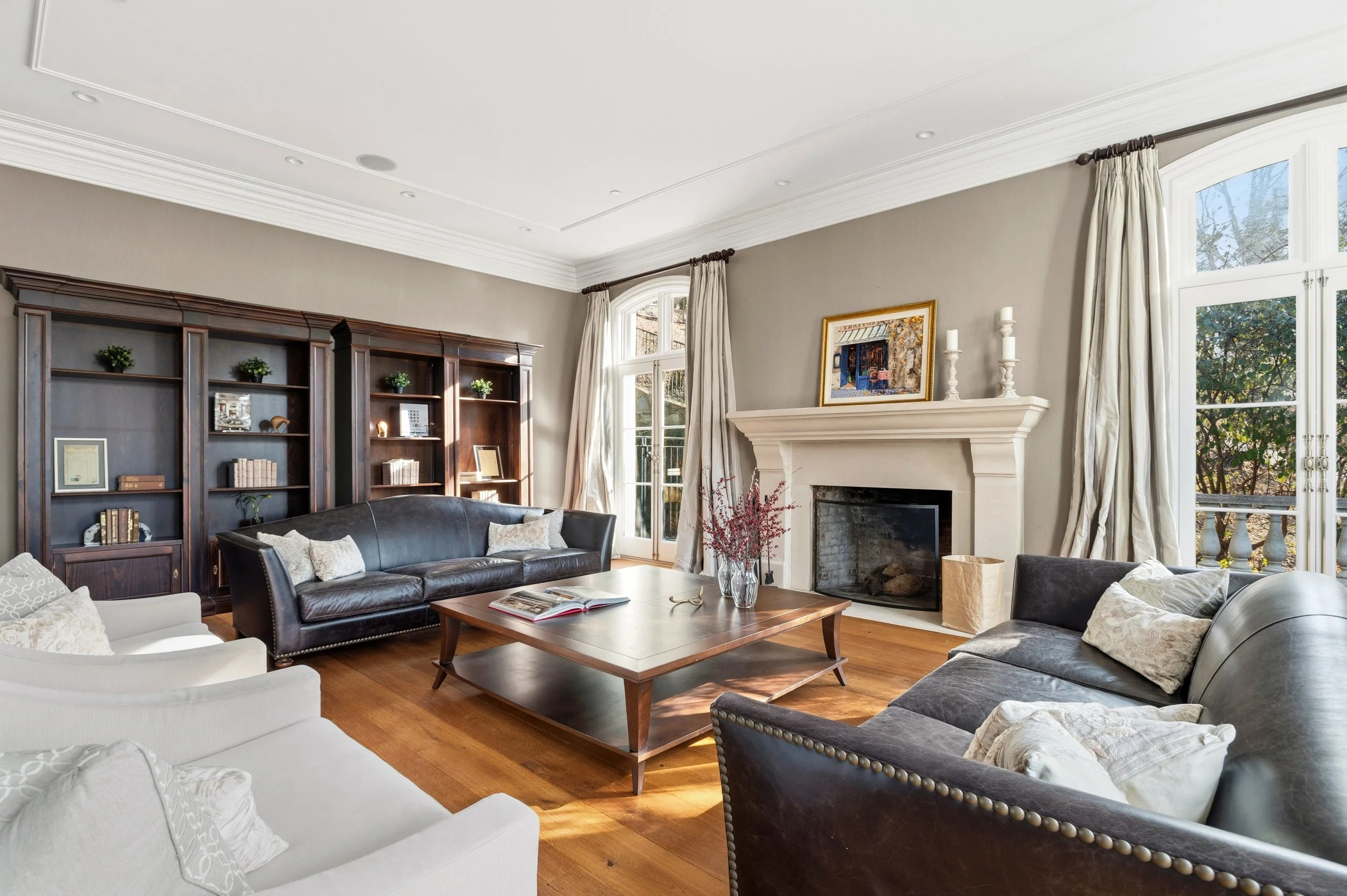 A spacious living room with large windows, a fireplace, wooden bookshelf, and various sofas and chairs around a wooden coffee table.