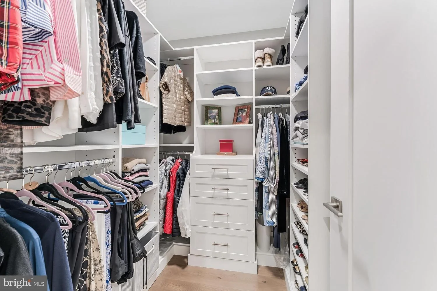 A spacious walk-in closet with white shelving and drawers, containing folded clothes, hanging garments, shoes, and accessories.