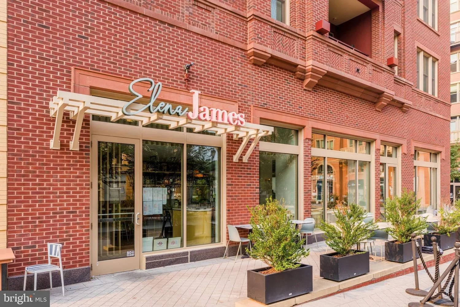 Exterior of a brick building with a sign reading 'Elen James', outdoor seating with potted plants