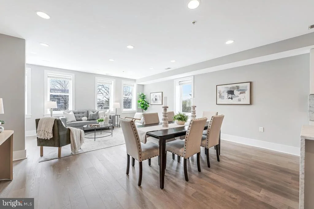 Bright, modern open-concept living and dining room with large windows, gray walls, beige accents, and minimalist decor.