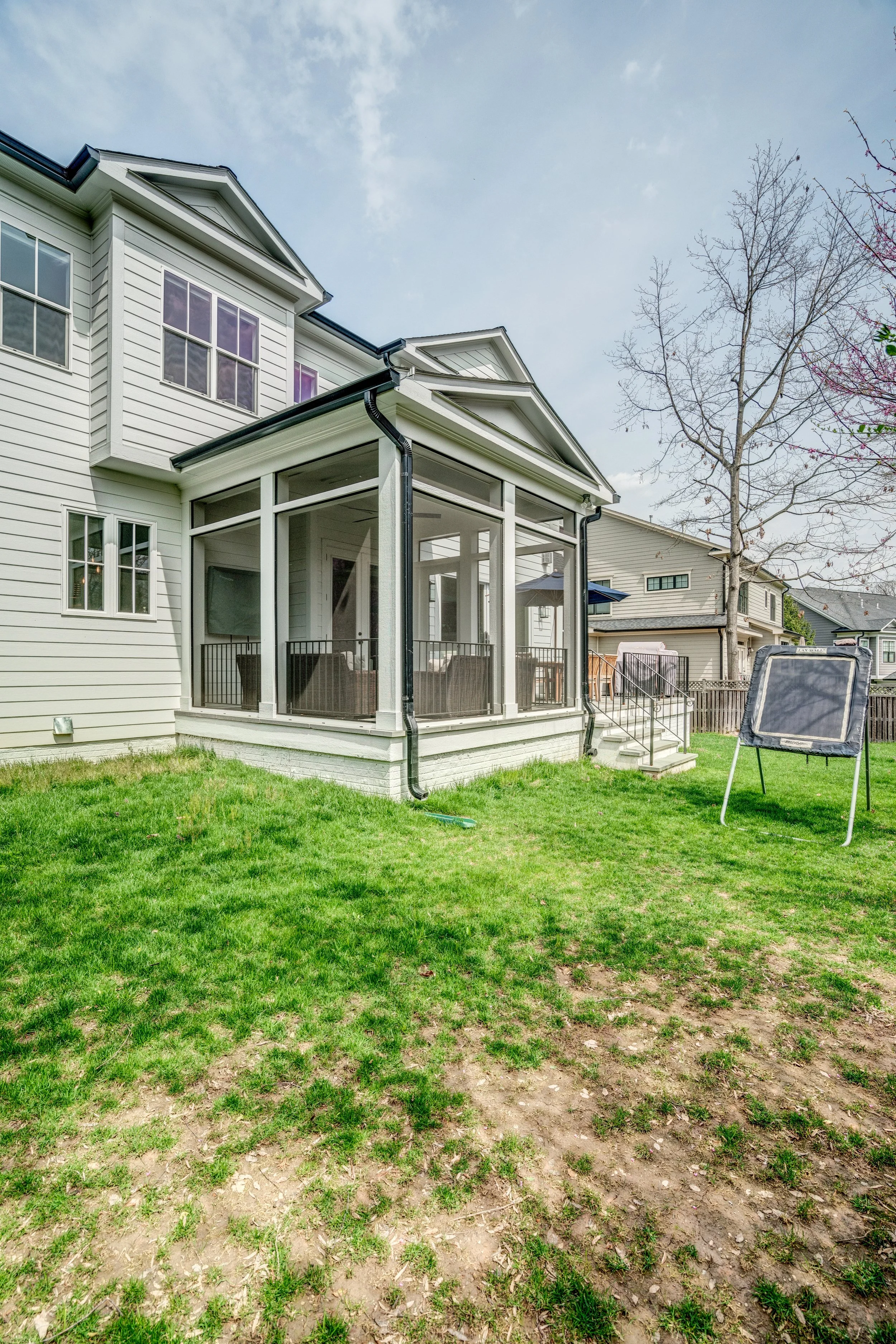Backyard with green grass, patches of dirt, a house with a screened-in porch, leafless tree, and a lawn chair in the yard.