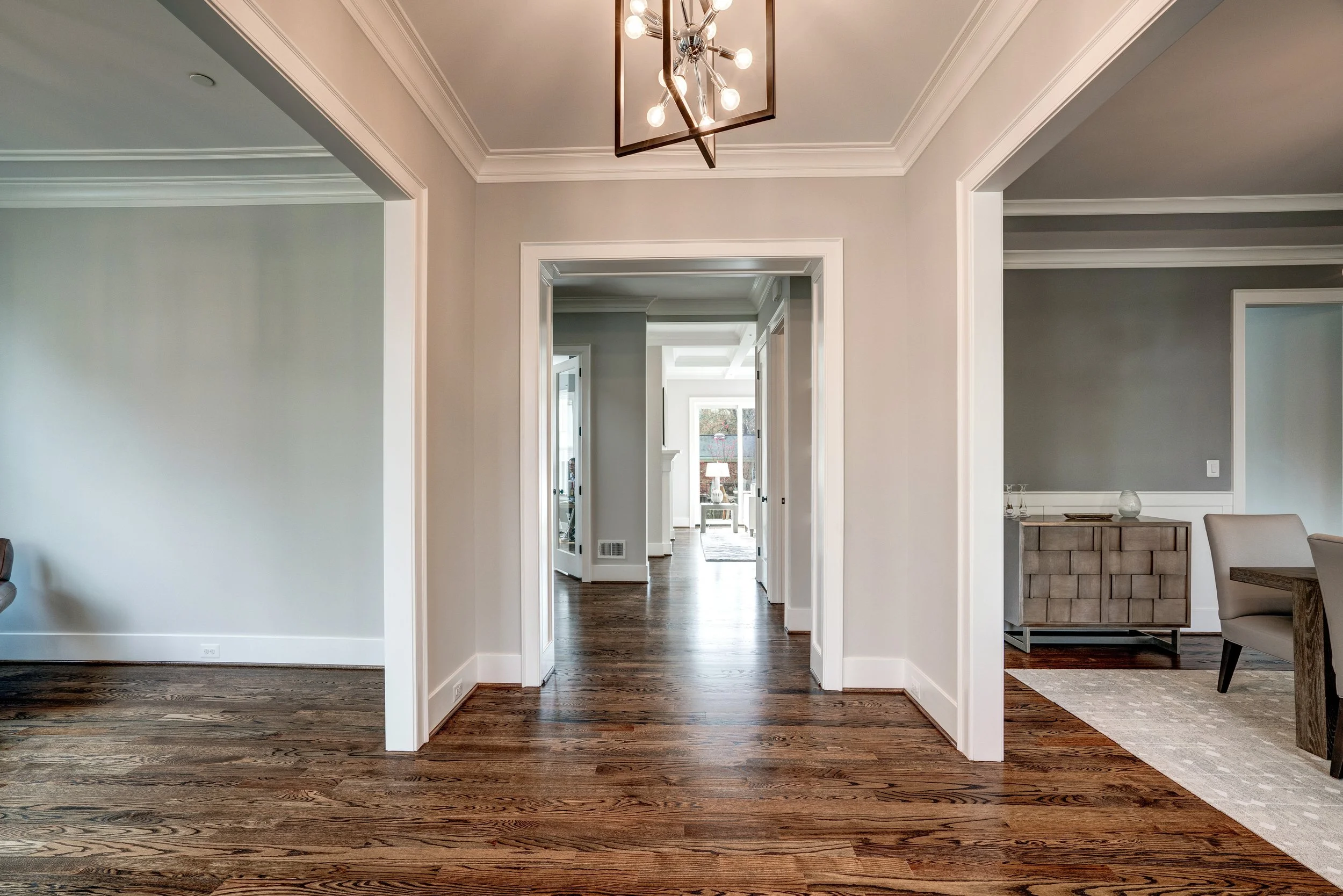 Interior view of a modern house with hardwood floors, multiple doorways, a chandelier, and a glimpse into other rooms.