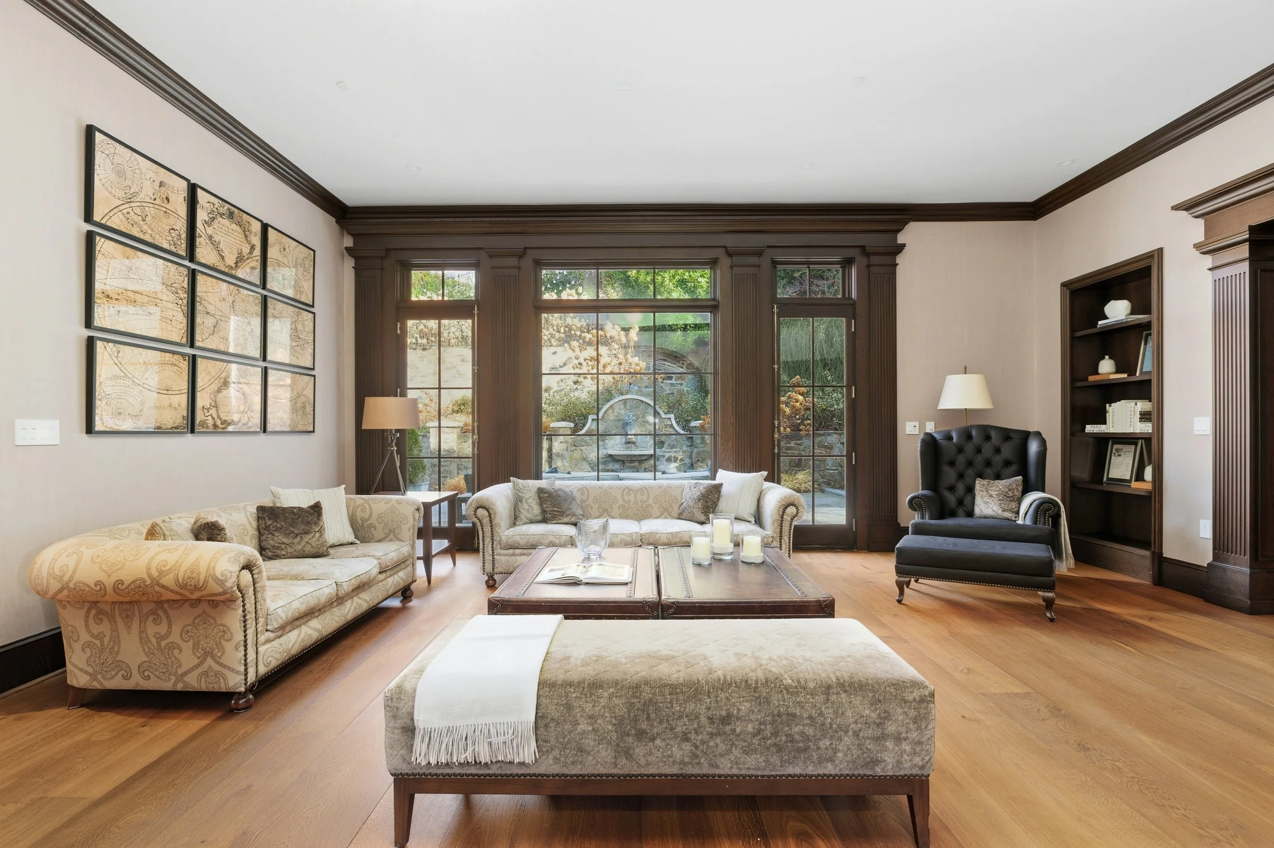 Living room with beige sofas, black armchair, wooden coffee table, windows with greenery outside, and artwork on the wall.