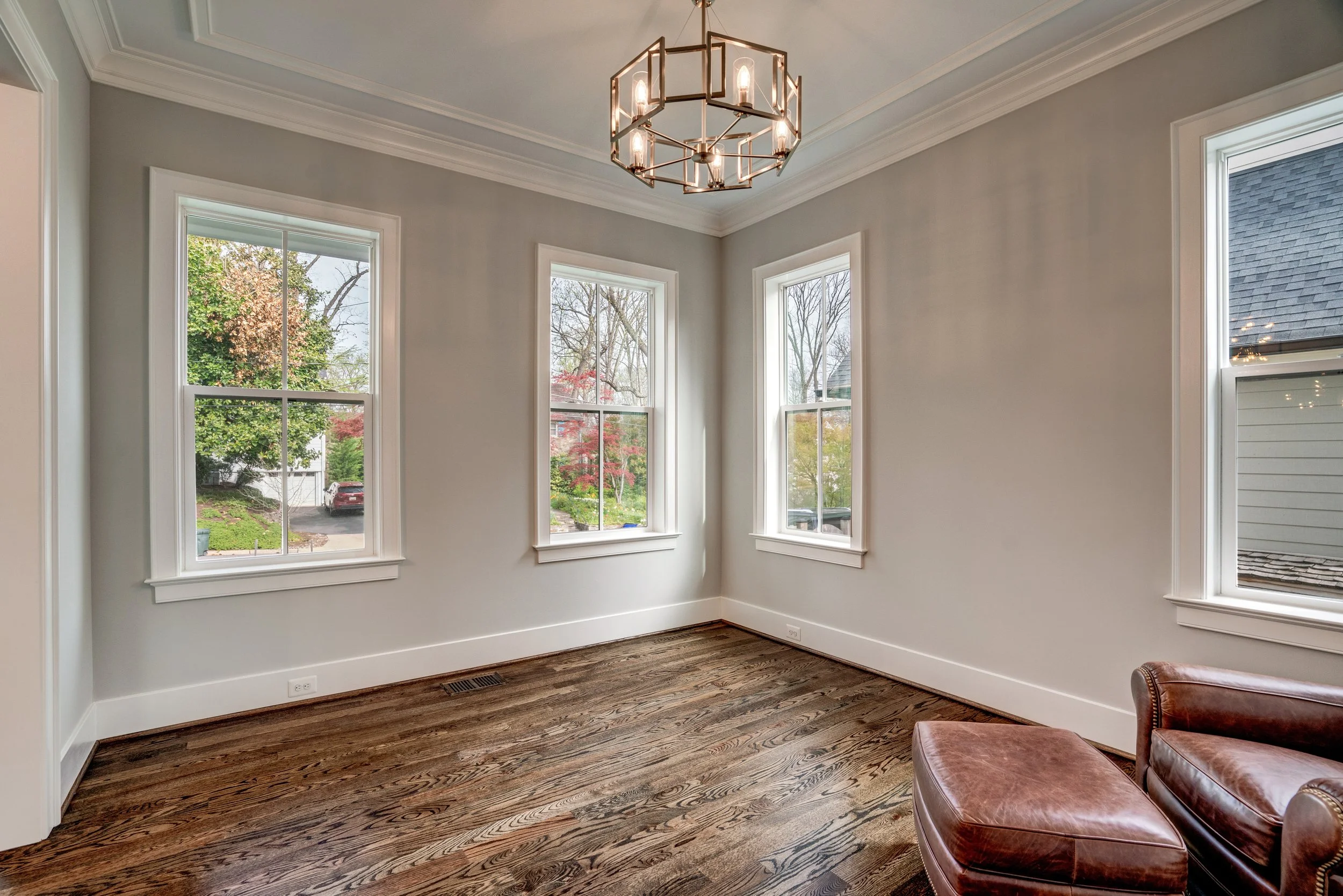 Empty living room with large windows, hardwood floors, and a modern chandelier