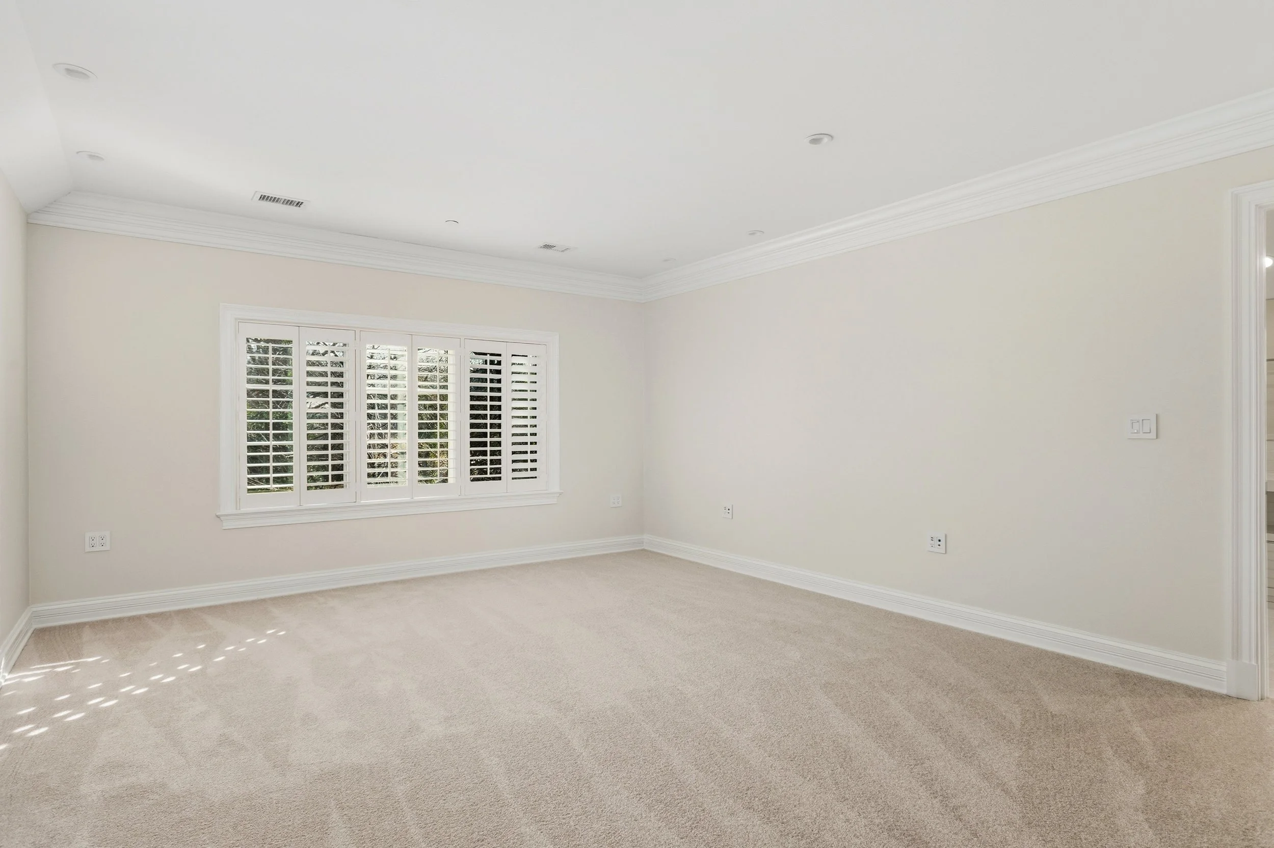 Empty room with beige carpeting, white walls, a window with shutters, and crown molding.
