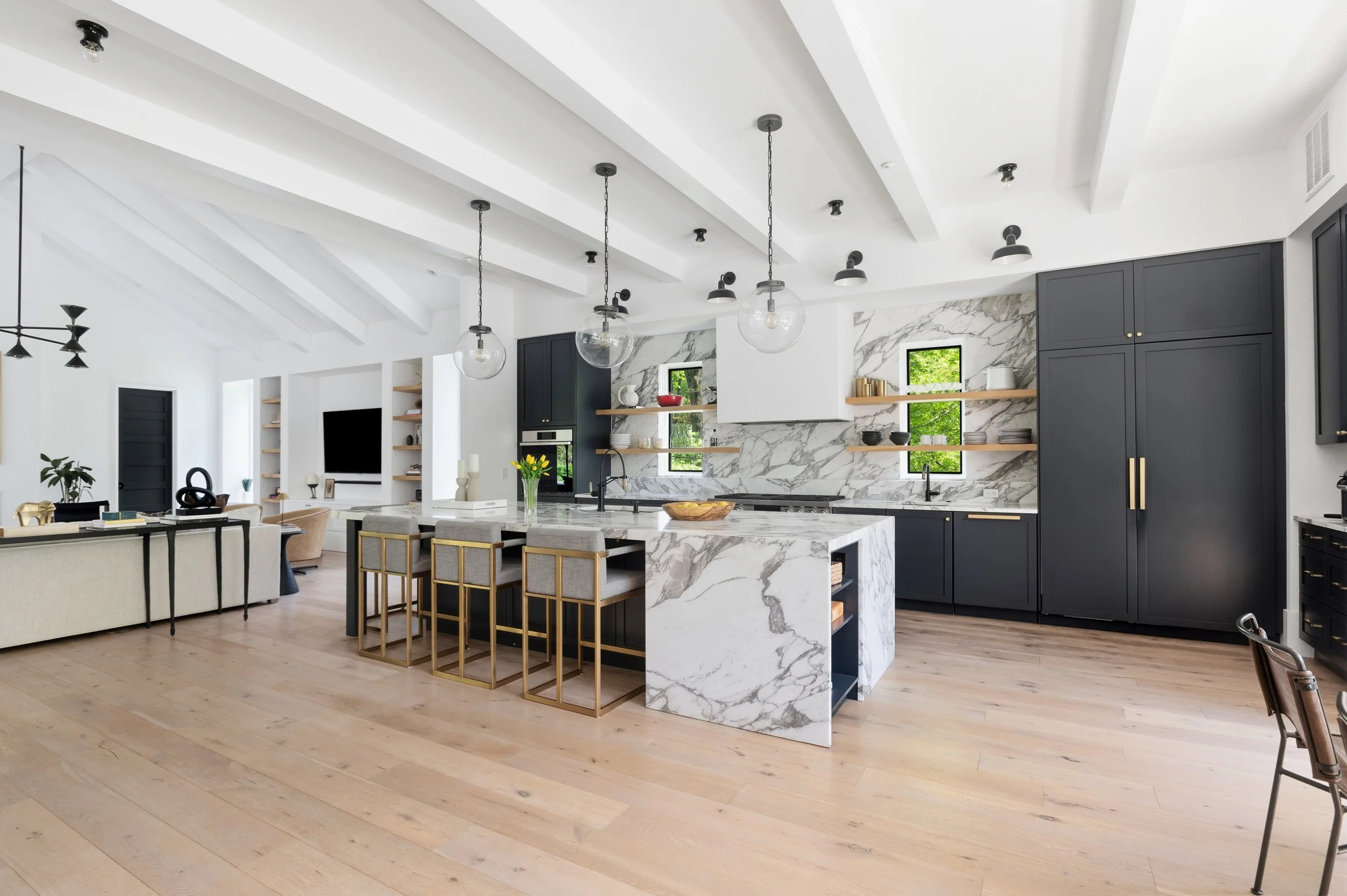 Modern open-plan kitchen with white walls, wooden floors, black and marble accents, and hanging globe pendant lights.