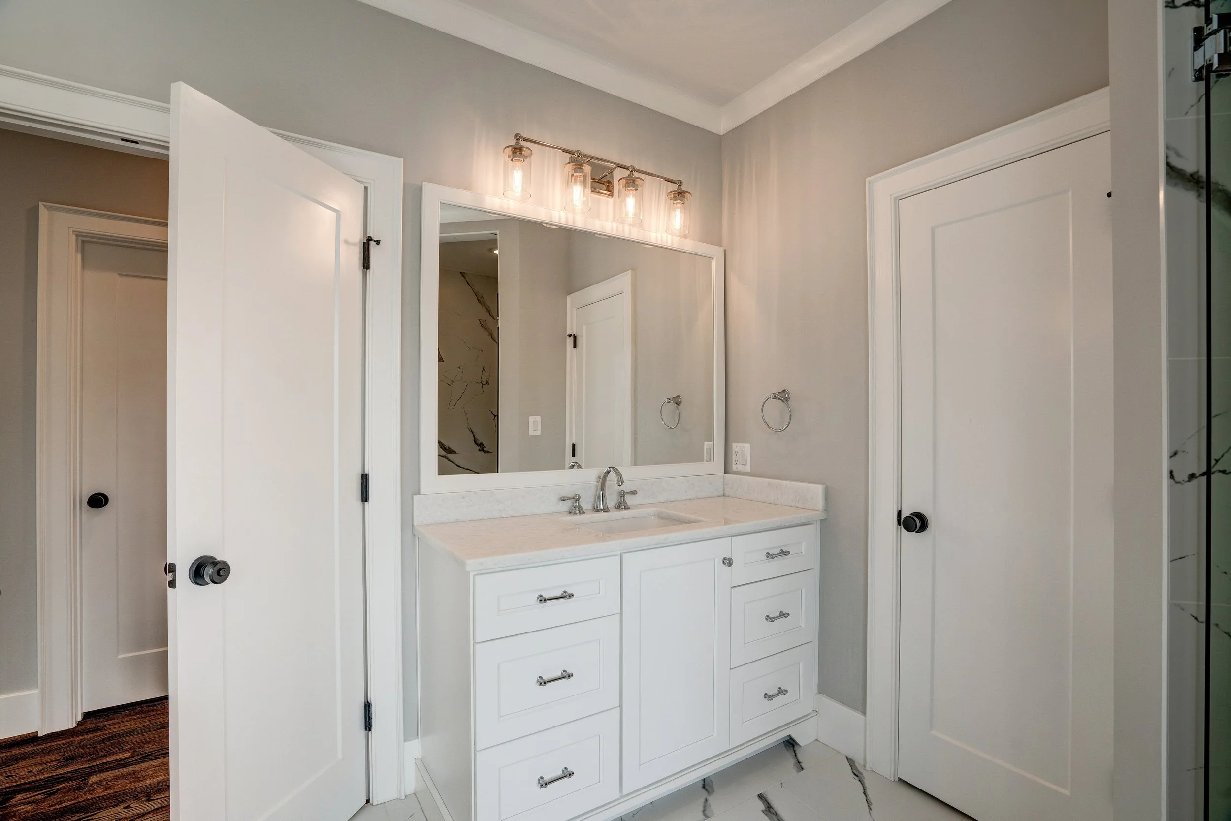 Bathroom vanity with a mirror, light fixture, sink, and white cabinetry, doors on either side, and a marble-tile floor.