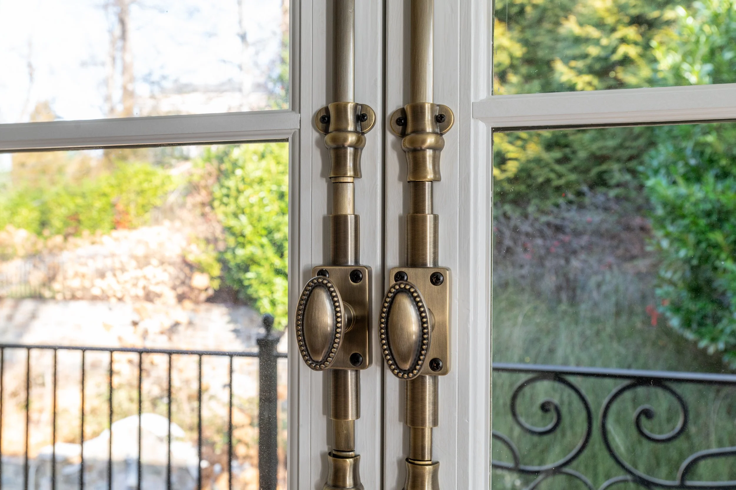 Close-up of brass door handles and lock on glass patio door with greenery outside.