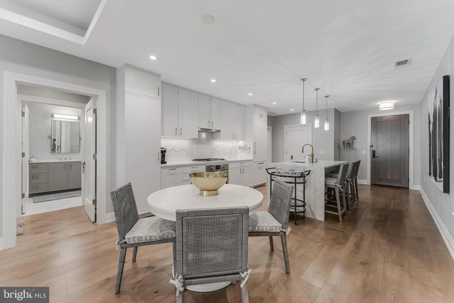 Modern kitchen with white cabinets, marble island, and dining area with four gray chairs, hardwood flooring, and contemporary pendant lighting.