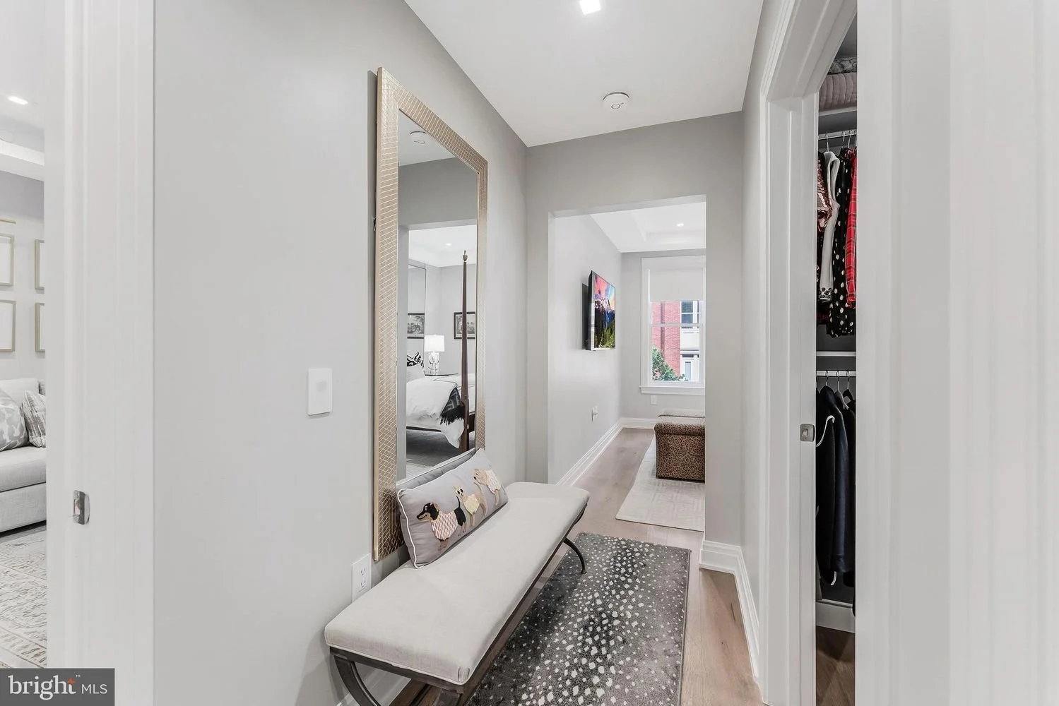 Entryway with a bench and a large wall mirror, leading to a living room with a TV and window, and a bedroom with a four-poster bed visible behind a doorway.