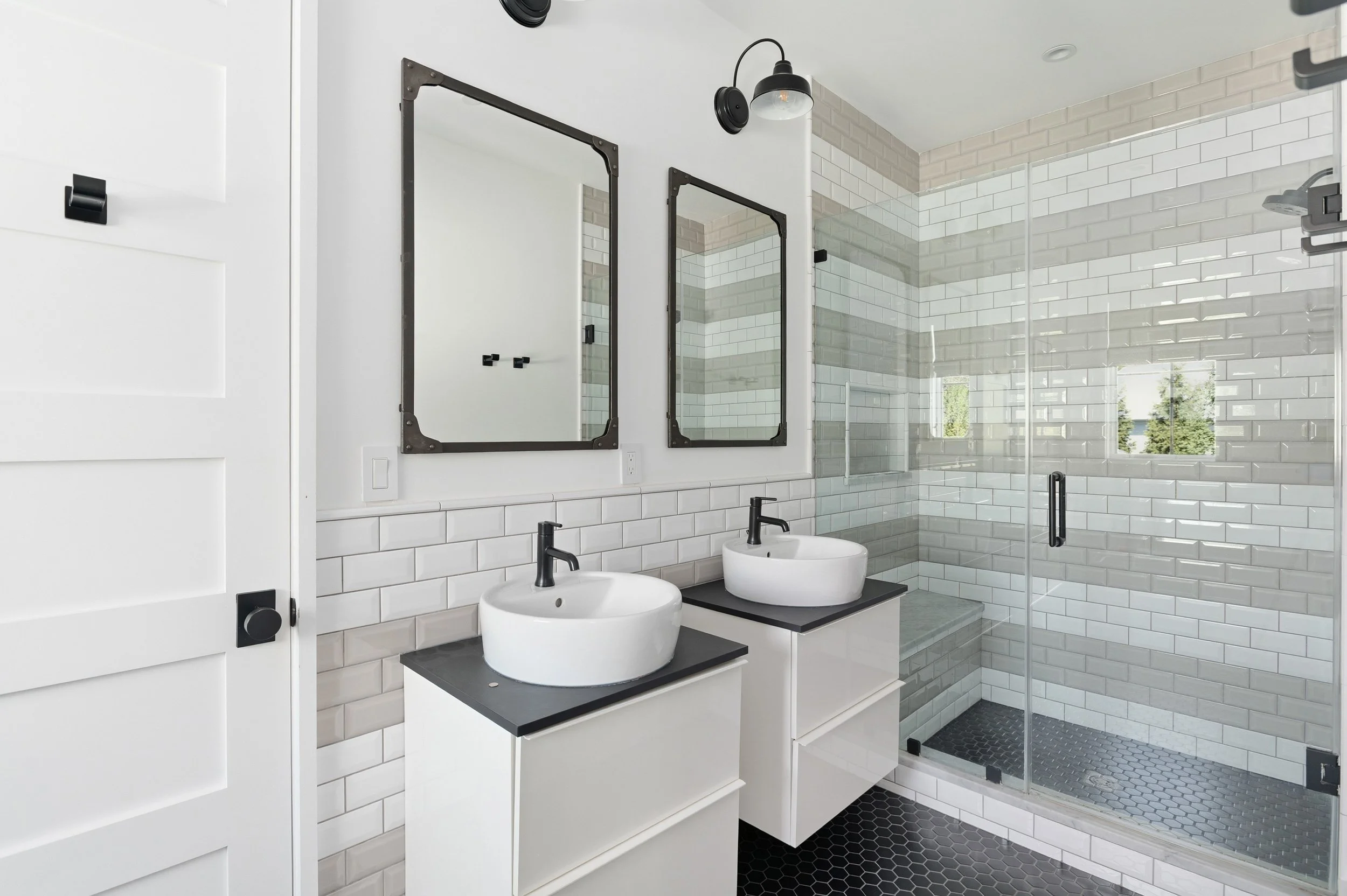 Modern bathroom with white subway tiles, black fixtures, dual sinks, large mirrors, and a glass-enclosed shower with black hardware.