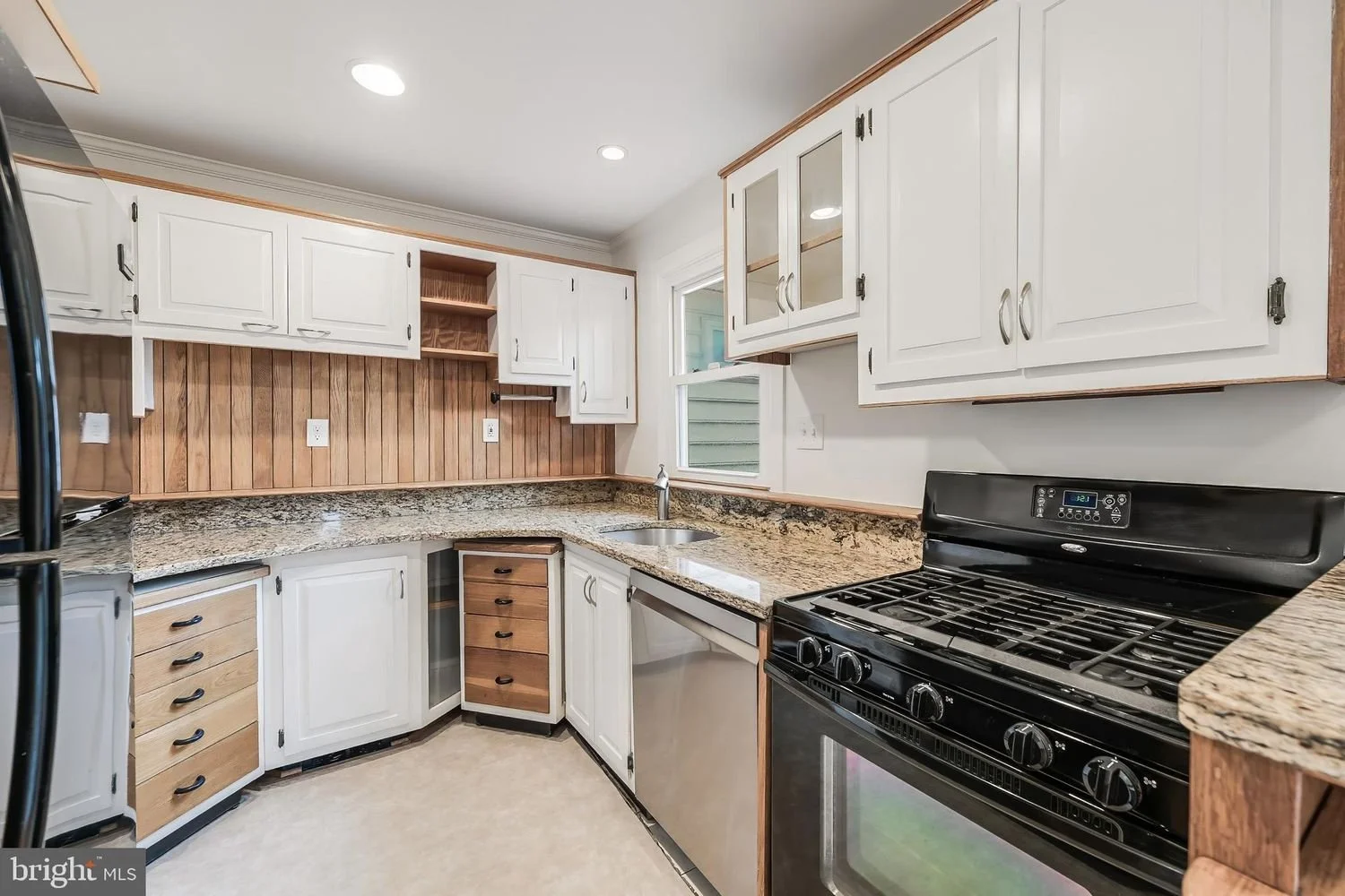 Kitchen with white cabinets, wooden accents, granite countertops, a black stove, a dishwasher, and a small window