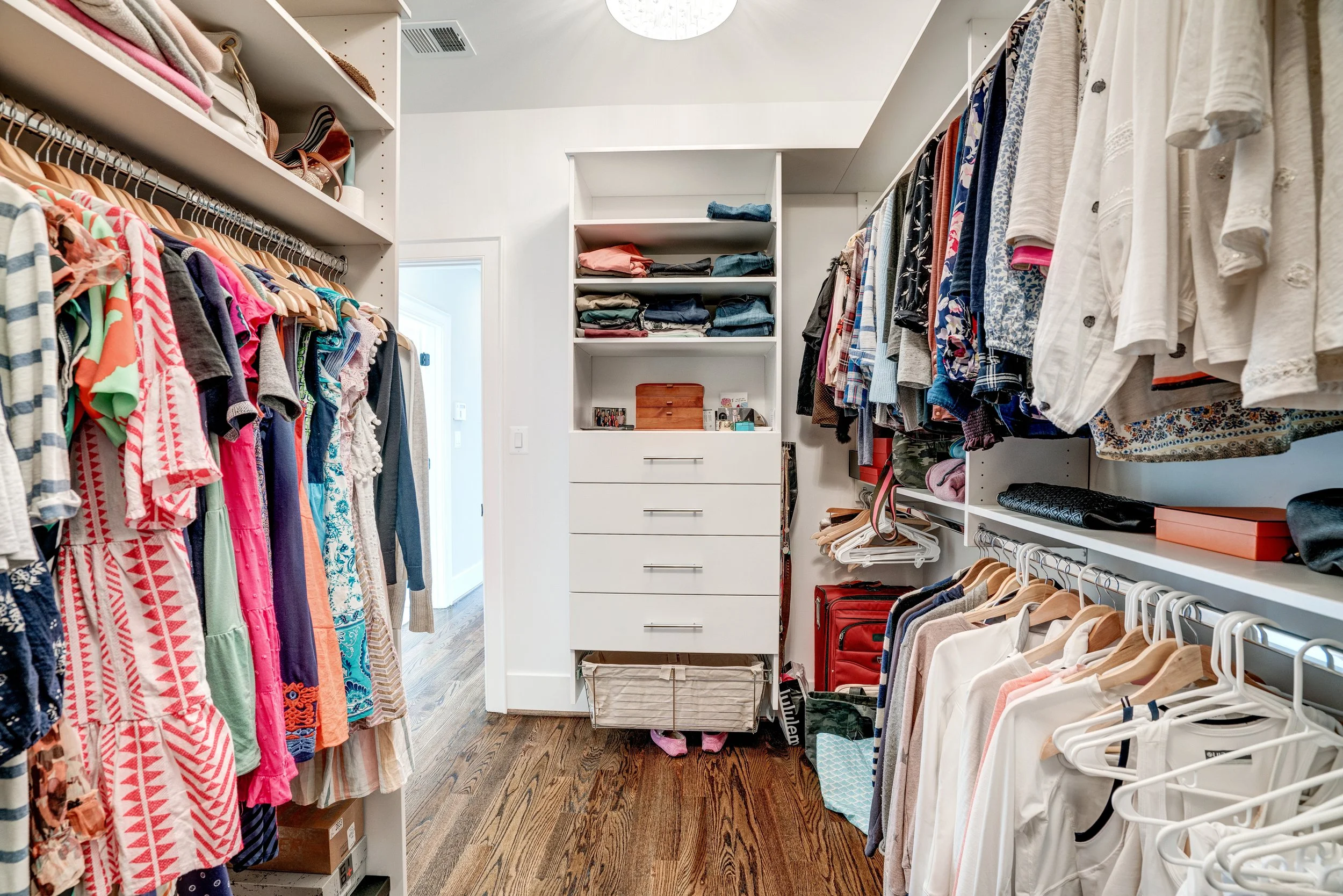 A walk-in closet with shelves and hanging space filled with various clothes, shoes, and accessories, with wood flooring and a white ceiling.