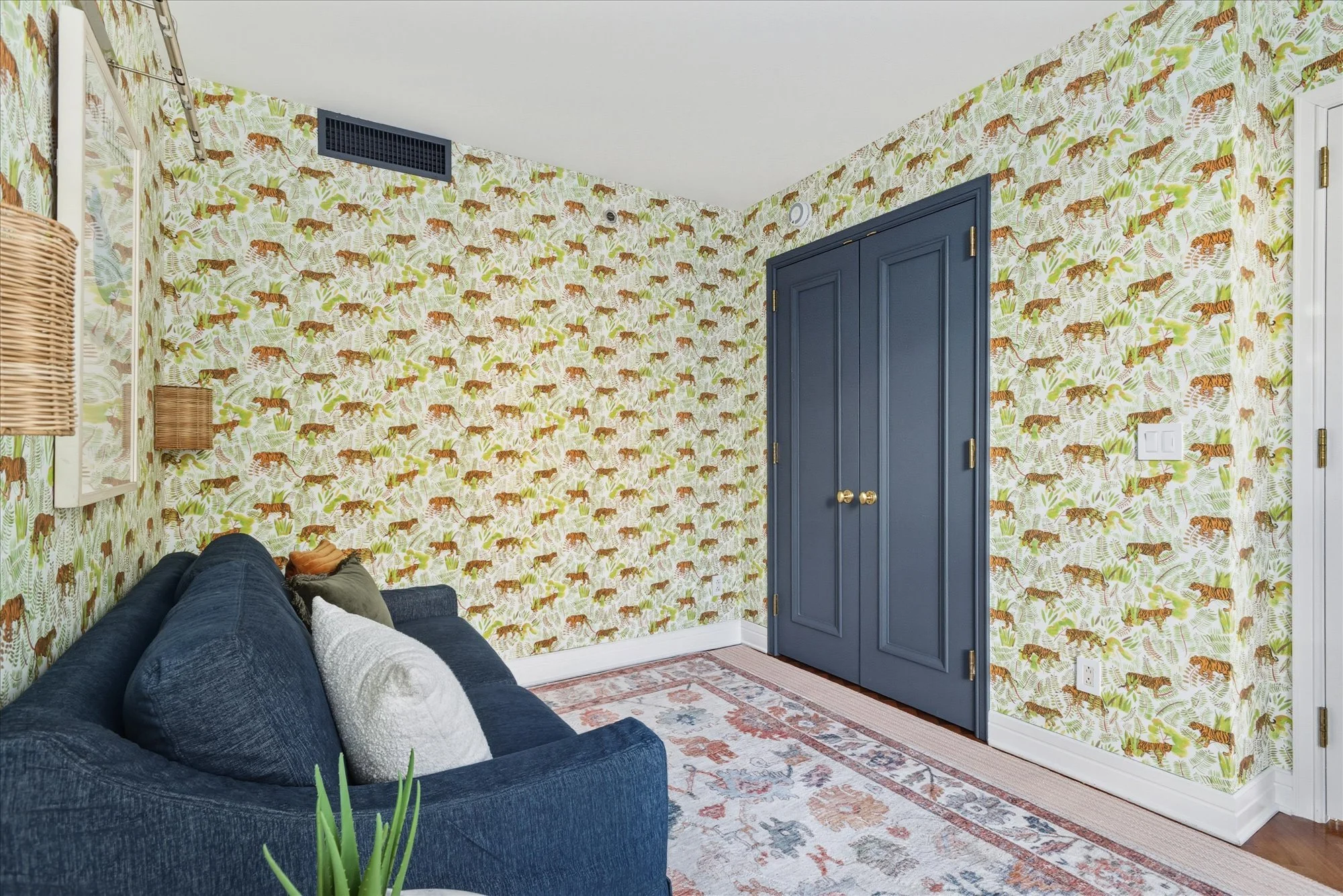 Room with jungle-themed wallpaper featuring tigers and green leaves, navy blue double doors, and a navy blue couch with pillows. A patterned rug is on the floor.